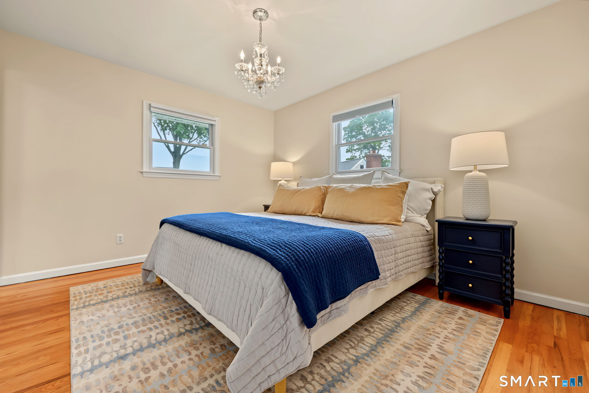 Furnished bedroom with a navy bedspread, two windows, and a crystal chandelier.