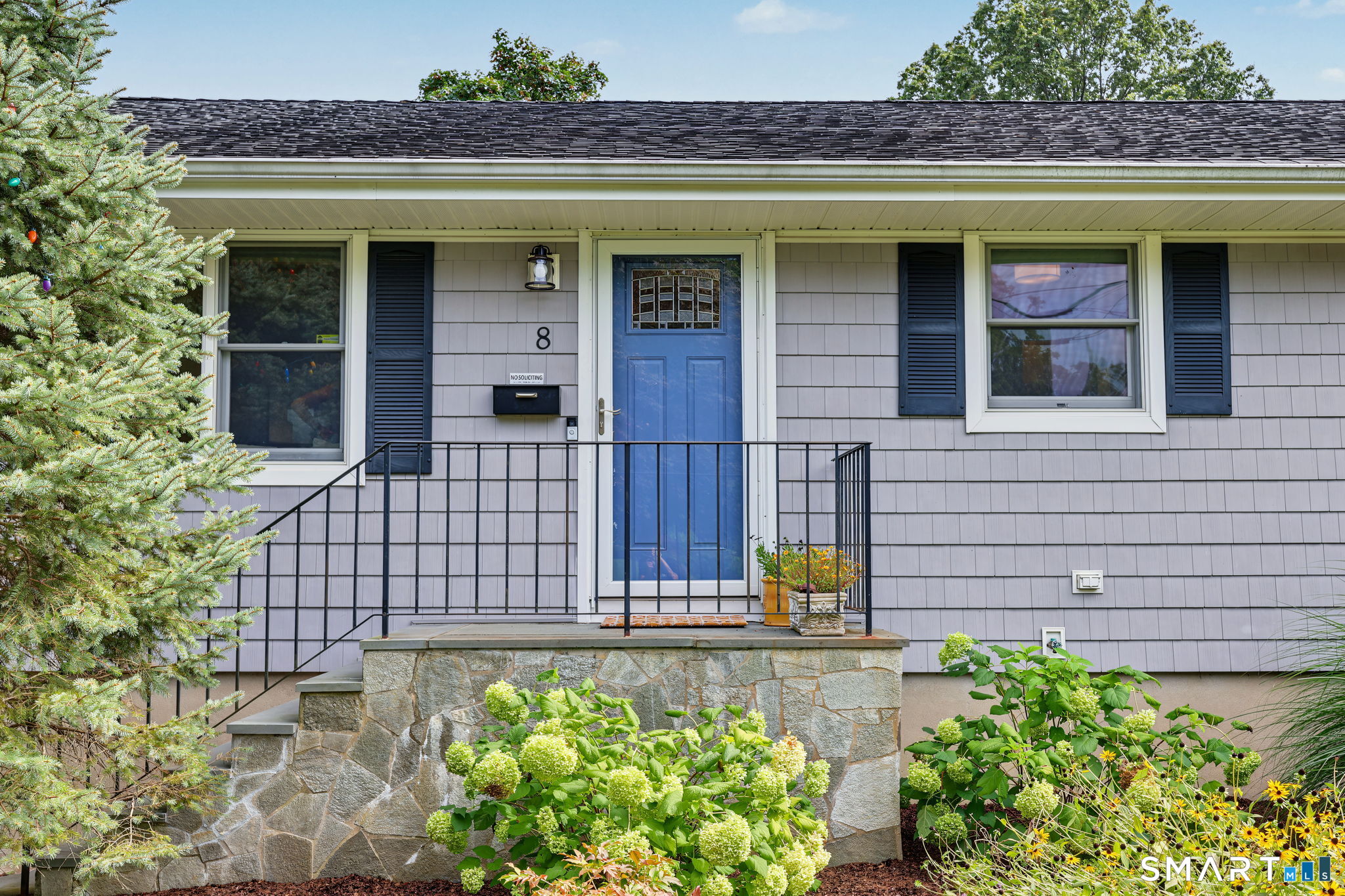 Home entrance with a blue door, raised stone porch, and flowering shrubs.