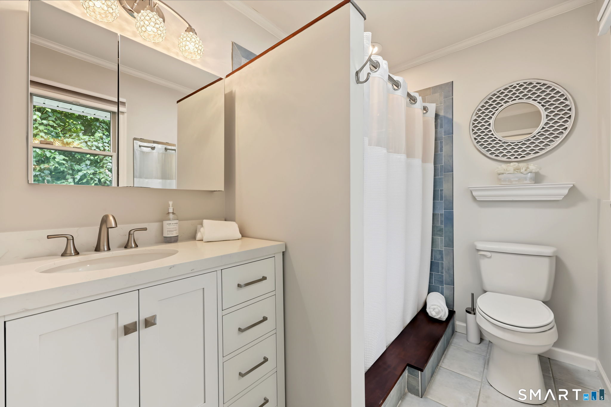 Bathroom with white vanity, blue-tiled shower, and toilet beneath an oval mirror.
