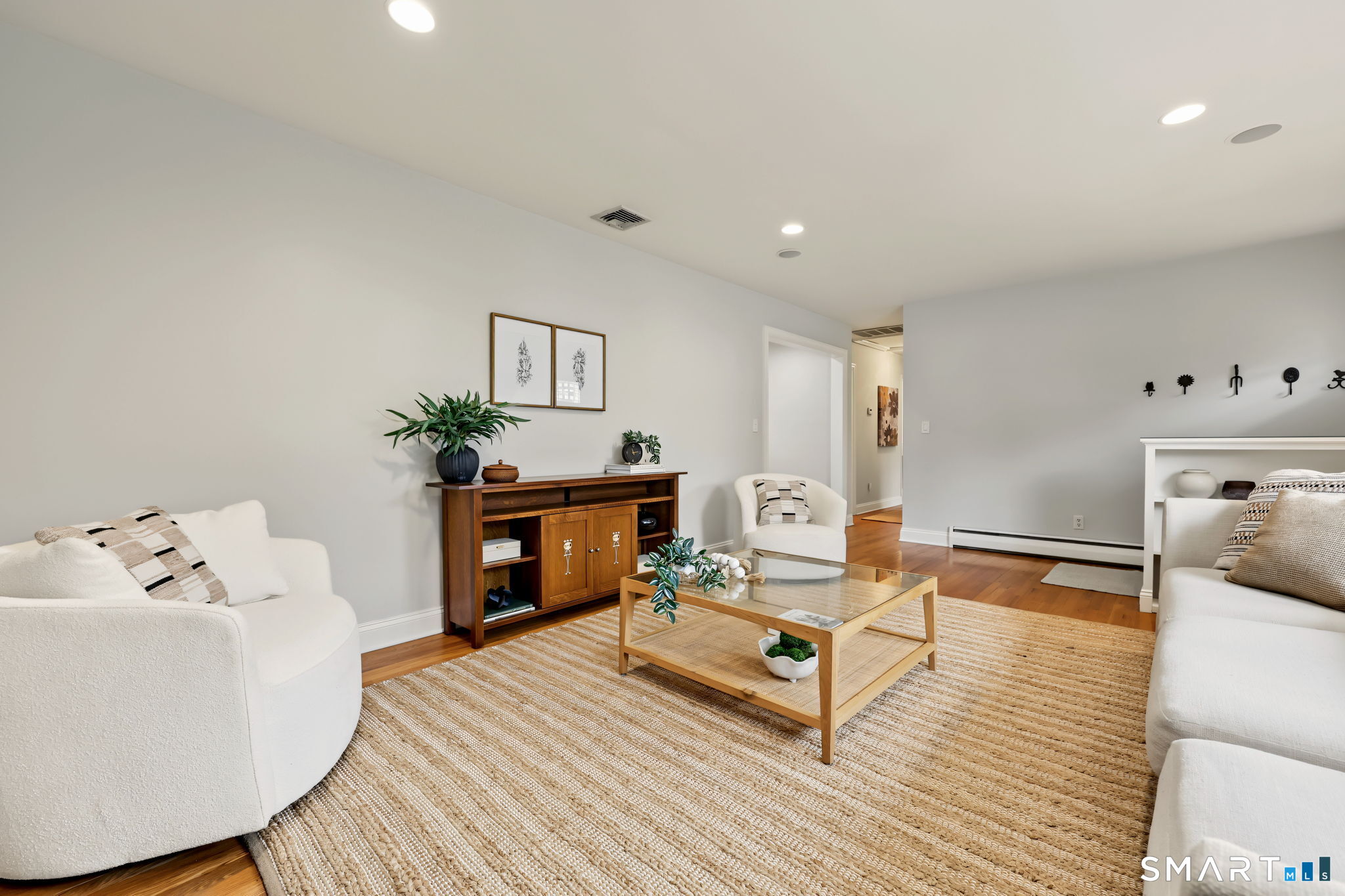 Staged living room with white sofas, a glass coffee table, and a large woven rug.
