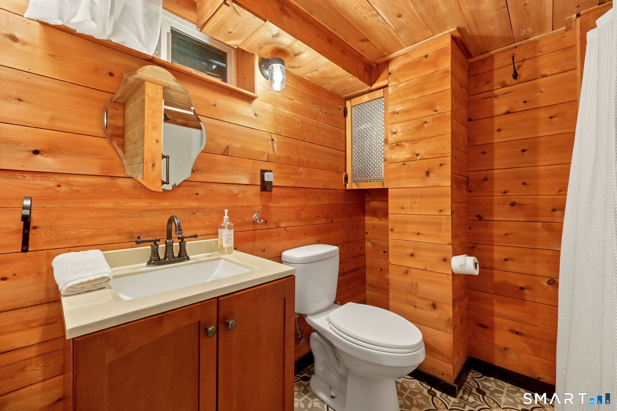 Wood-paneled bathroom with a cream sink vanity, white toilet, and patterned tile floor.