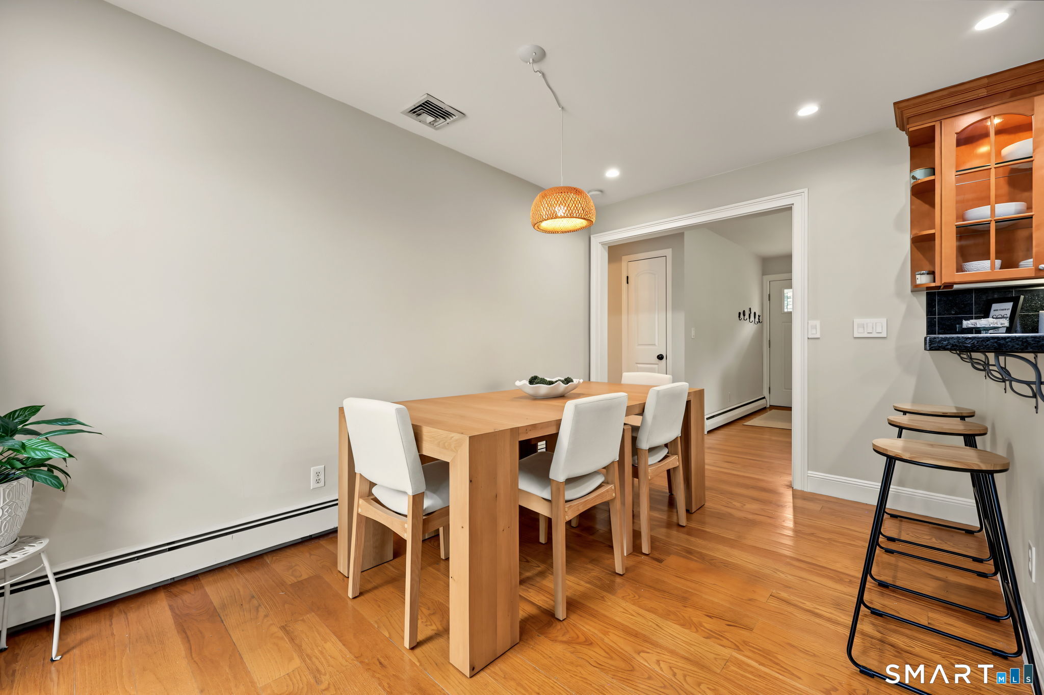 Dining area with a light wood table, white chairs, hardwood floors, and a breakfast counter with stools.