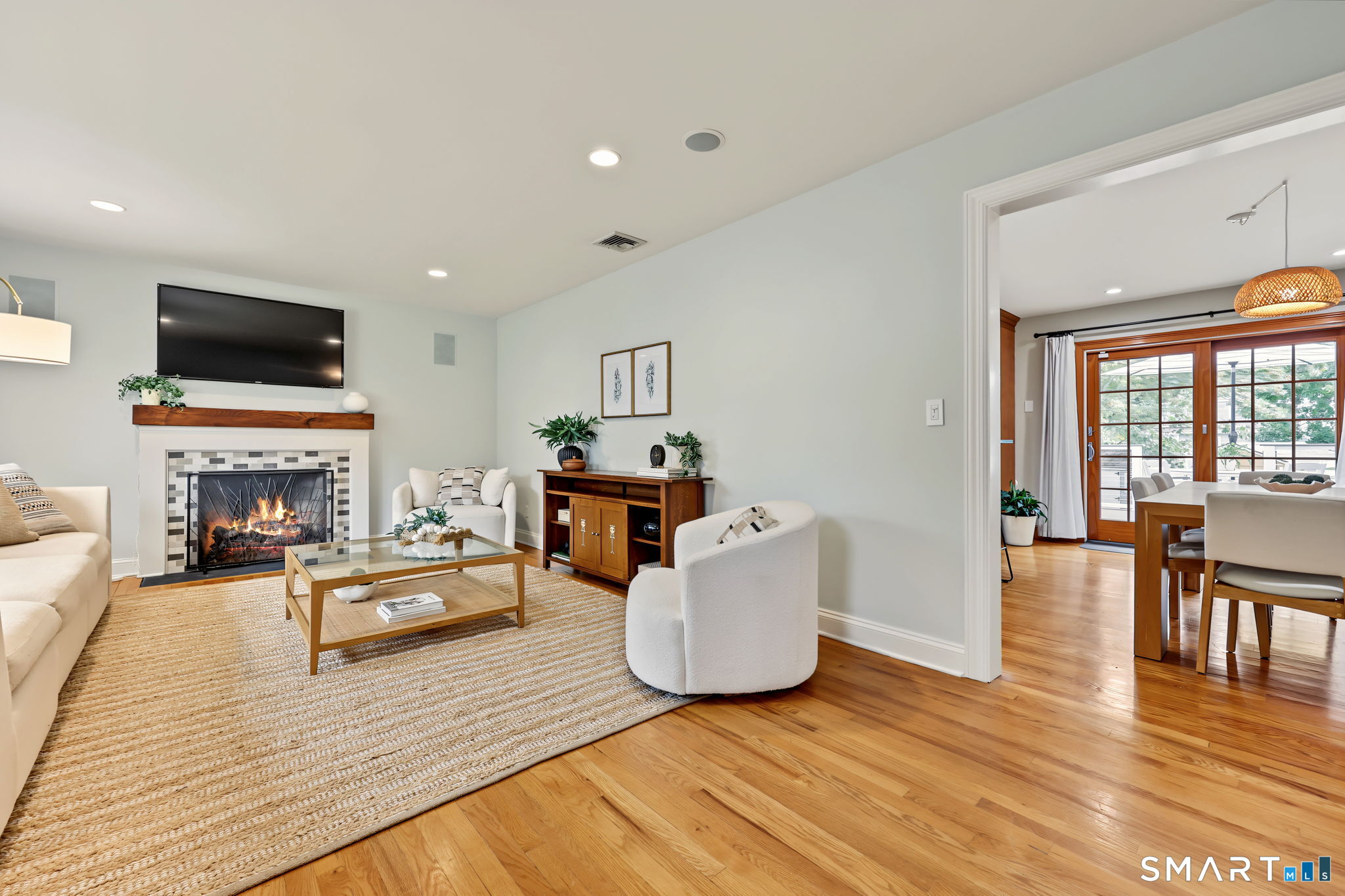 Staged living room with a tiled fireplace and cream seating, opening to a dining area with glass doors.