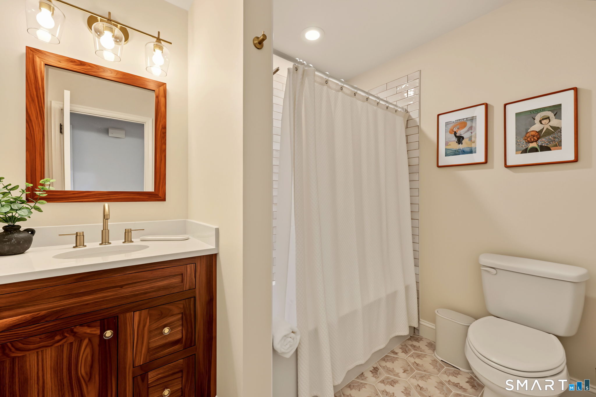 Bathroom with a dark wood vanity, white shower curtain, framed prints, and patterned floor tile.