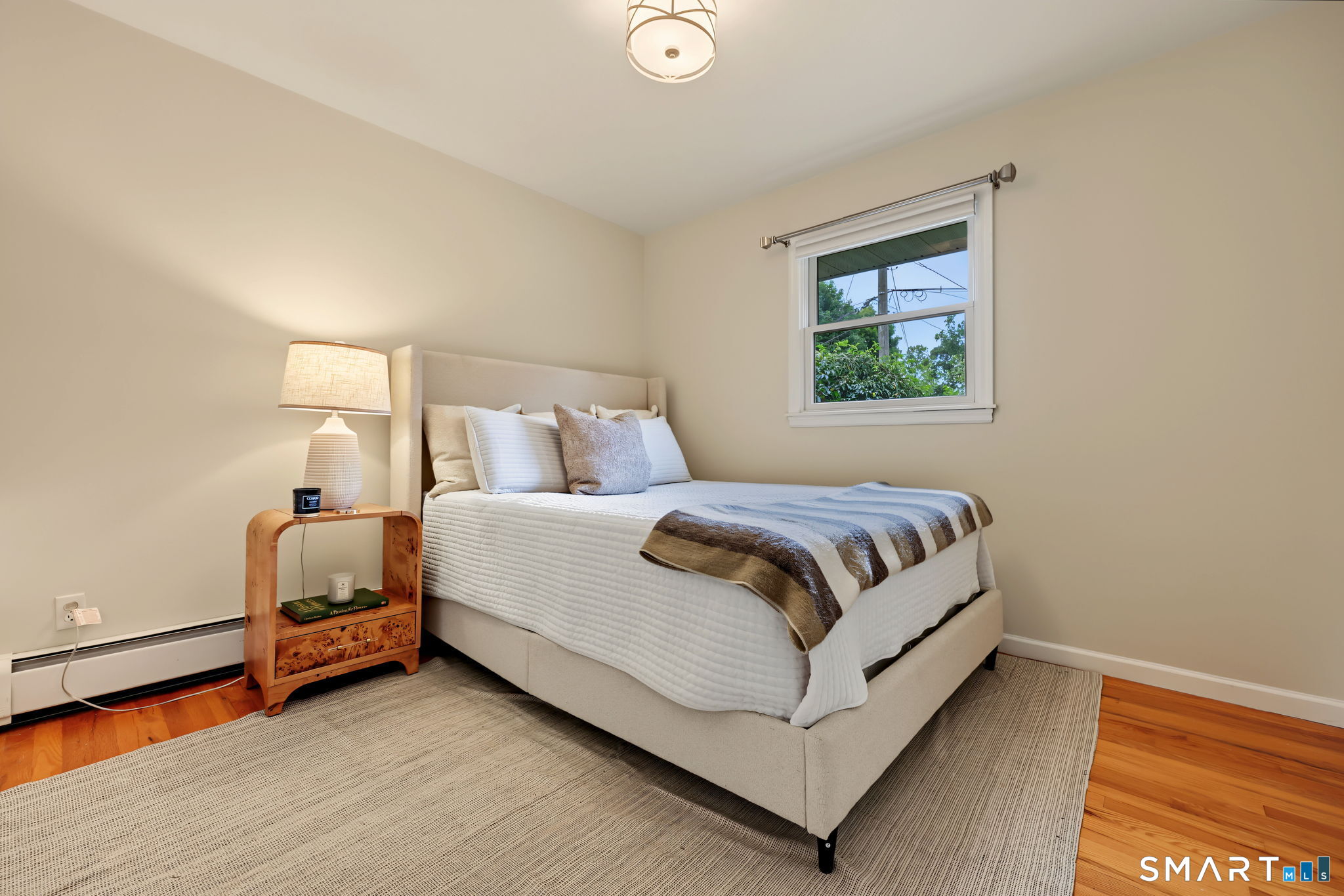 Staged bedroom with a beige upholstered bed, white bedding, and hardwood floors.