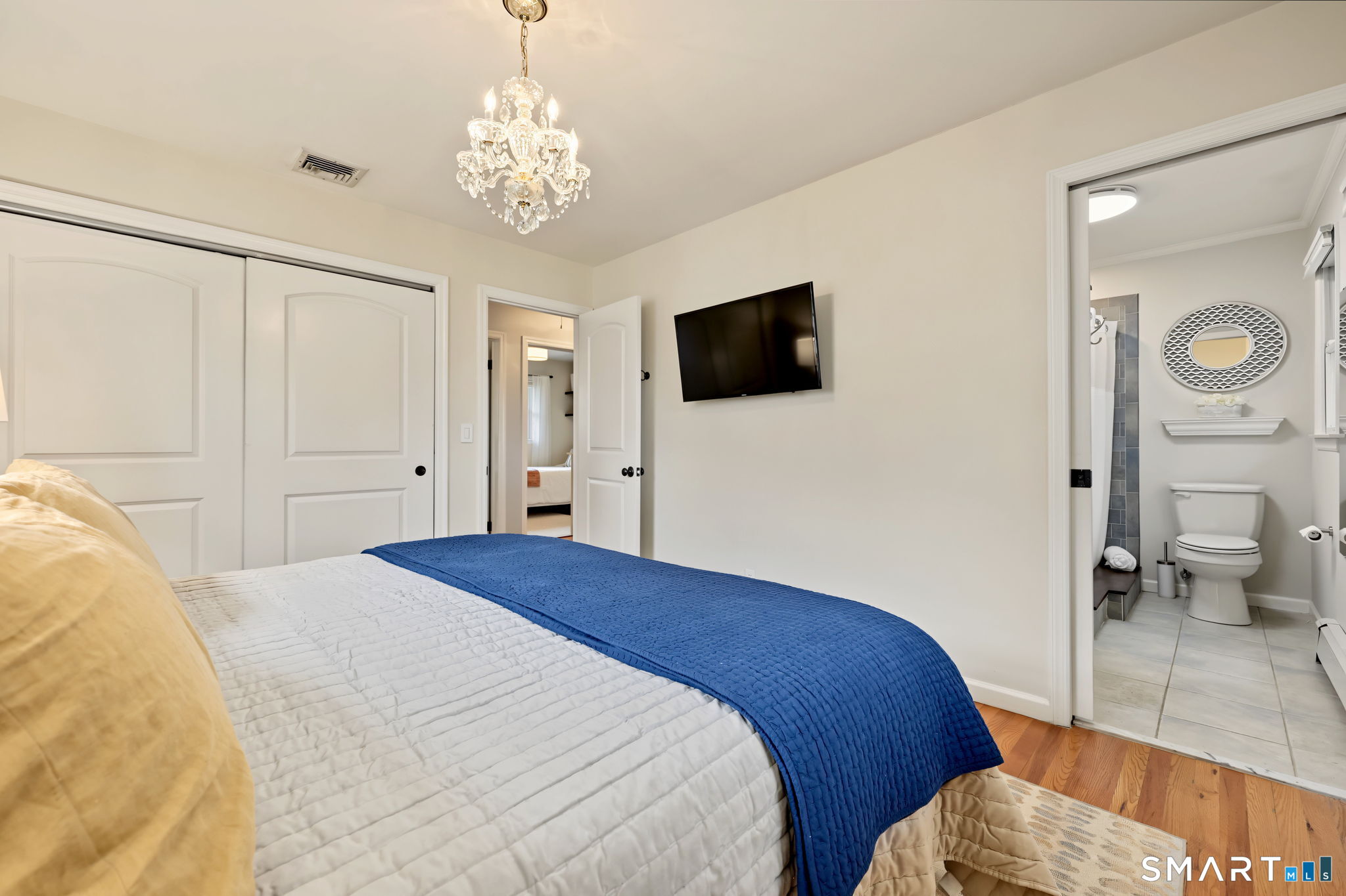 Bedroom with a blue quilted bed, chandelier, and adjoining bathroom.