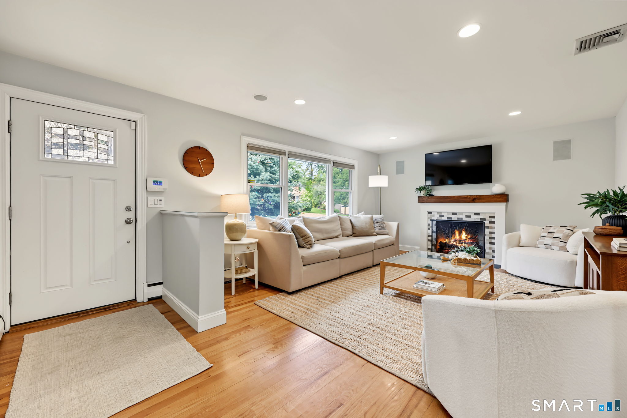 Furnished living room with a lit fireplace, neutral sofas, and large windows.