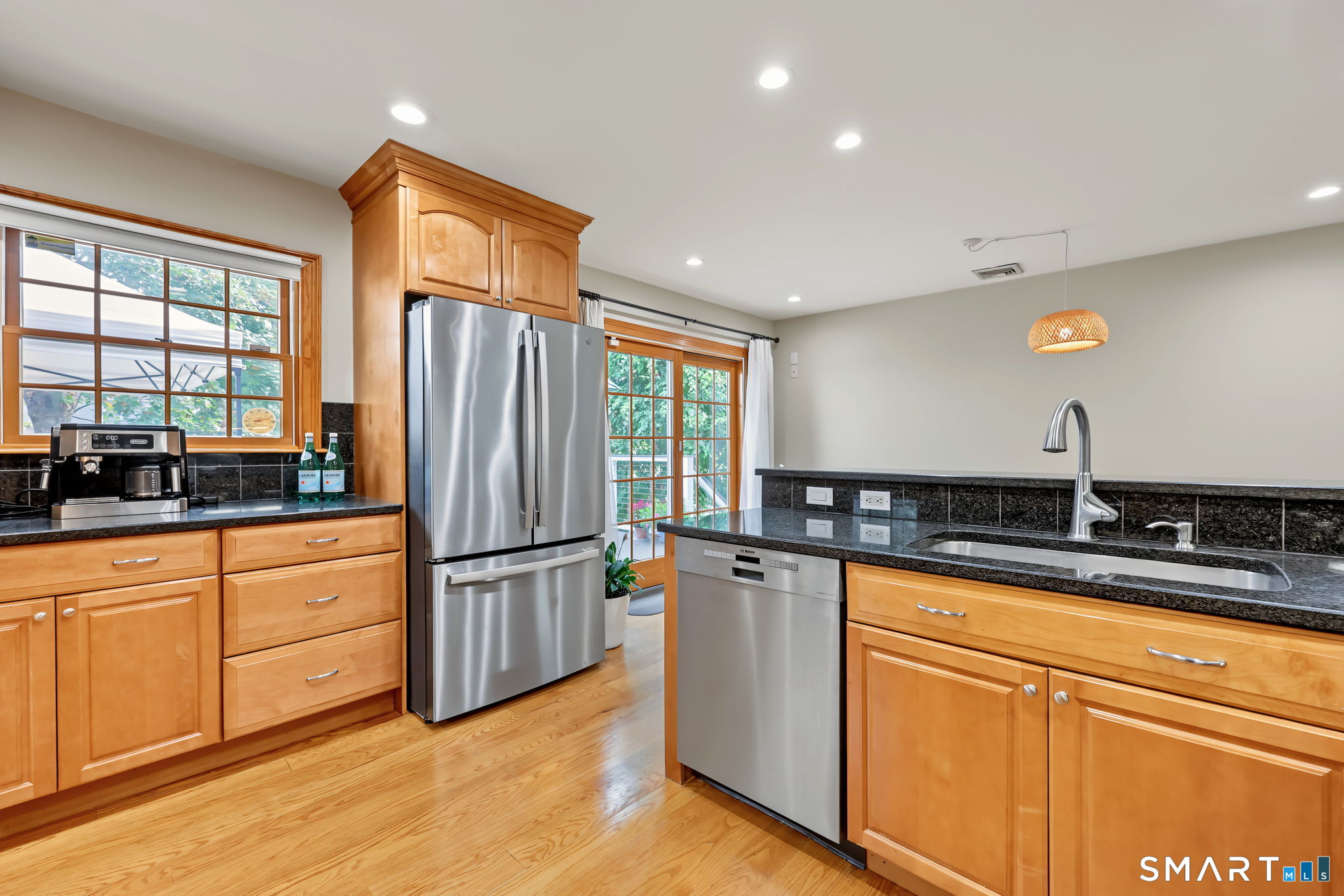 Kitchen with honey-colored wood cabinets, black stone countertops, stainless steel appliances, and hardwood floors.