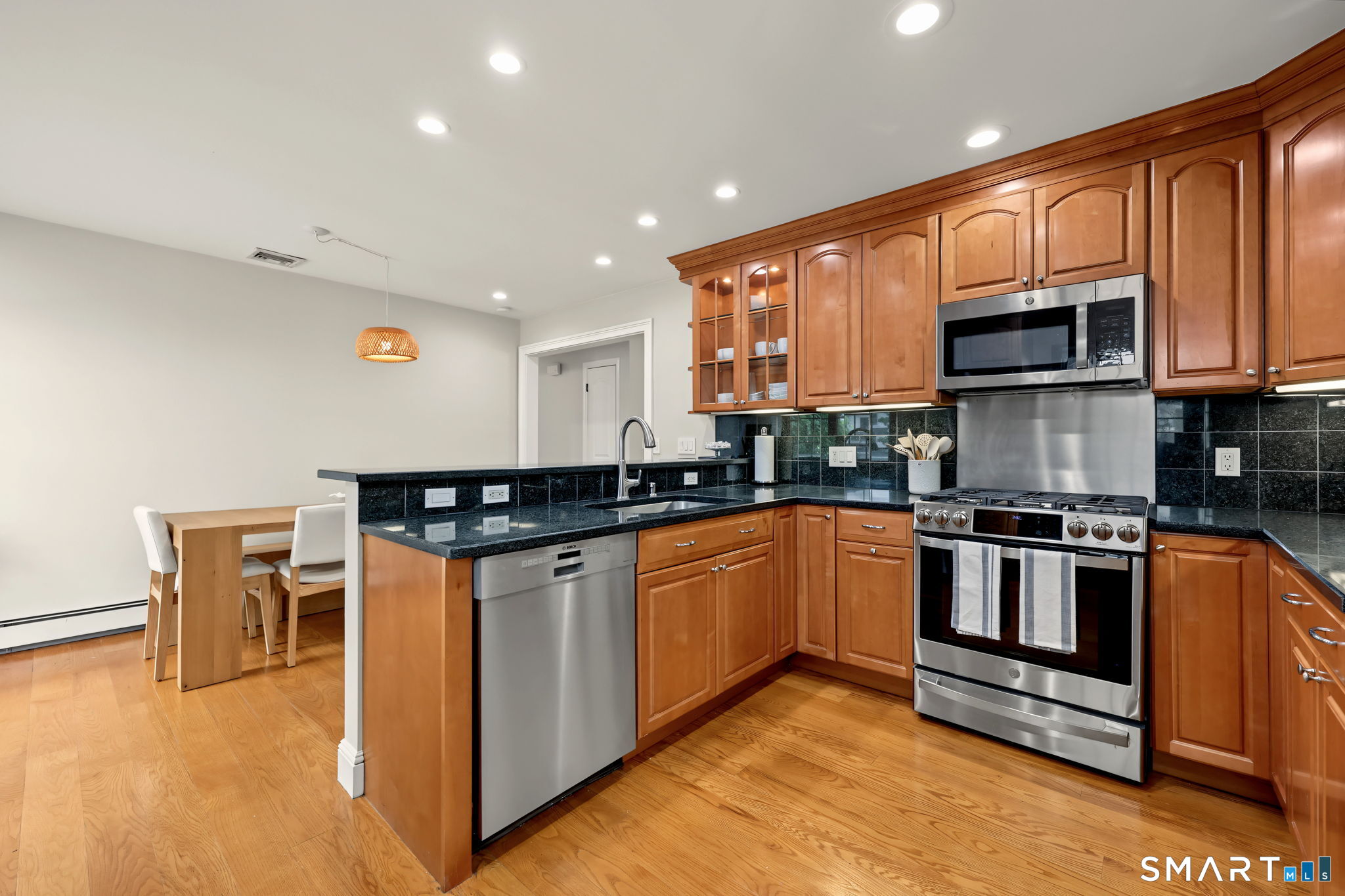 Kitchen with wood cabinets, black counters, stainless steel appliances, and an adjoining dining table.