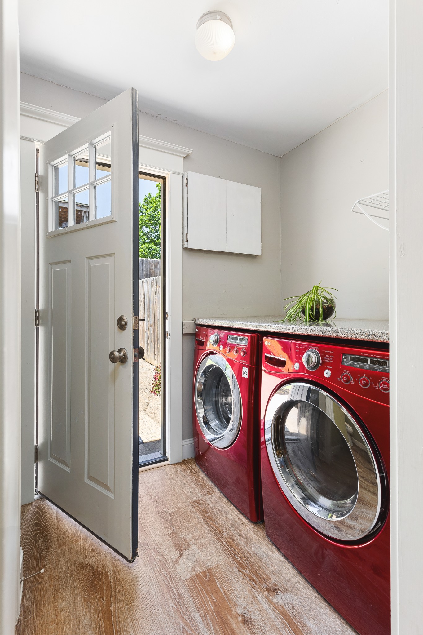 Laundry room with red front-loading washer and dryer, a speckled counter, and an open exterior door.