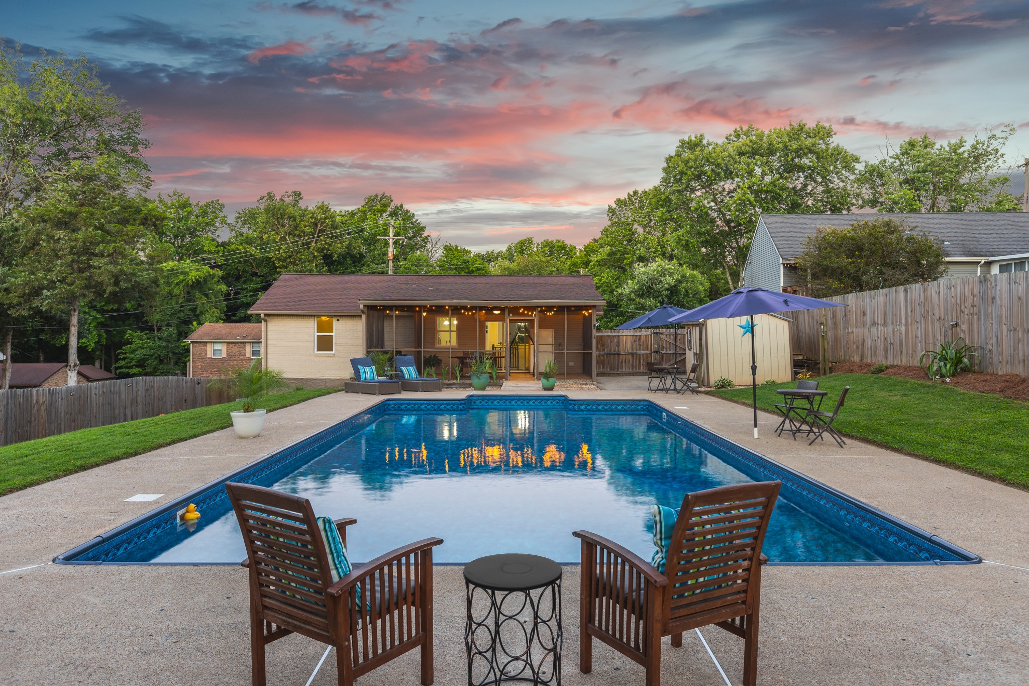 Backyard swimming pool facing a screened porch at dusk, with patio seating.