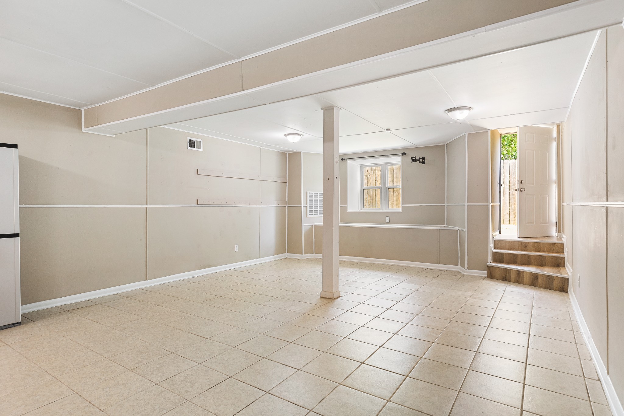 Empty tiled room with a support column and steps leading to an open door.