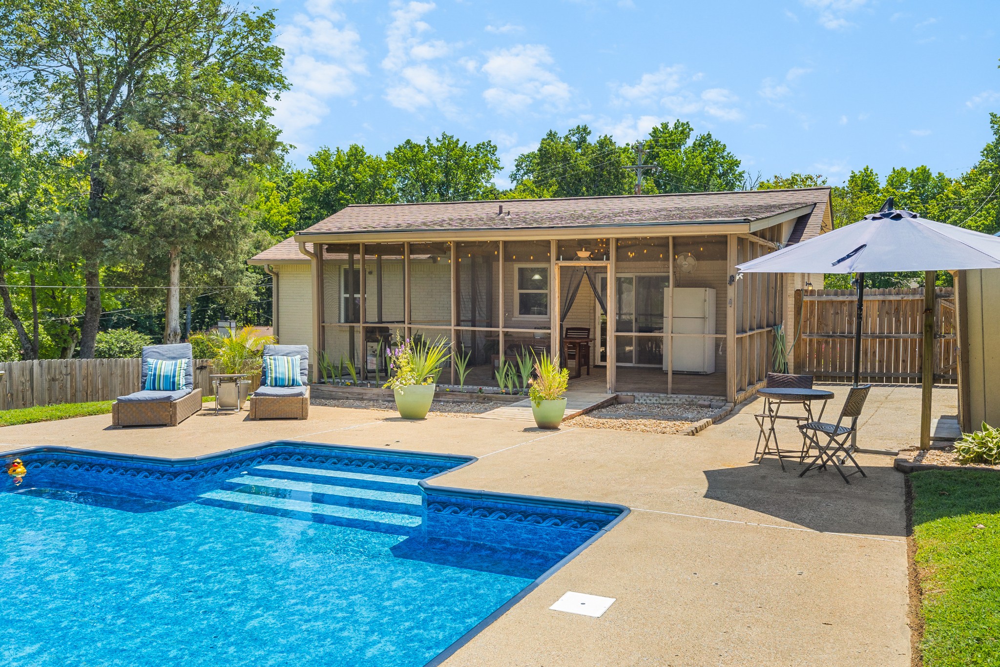 Backyard swimming pool and patio with screened porch, outdoor chairs, and umbrella.