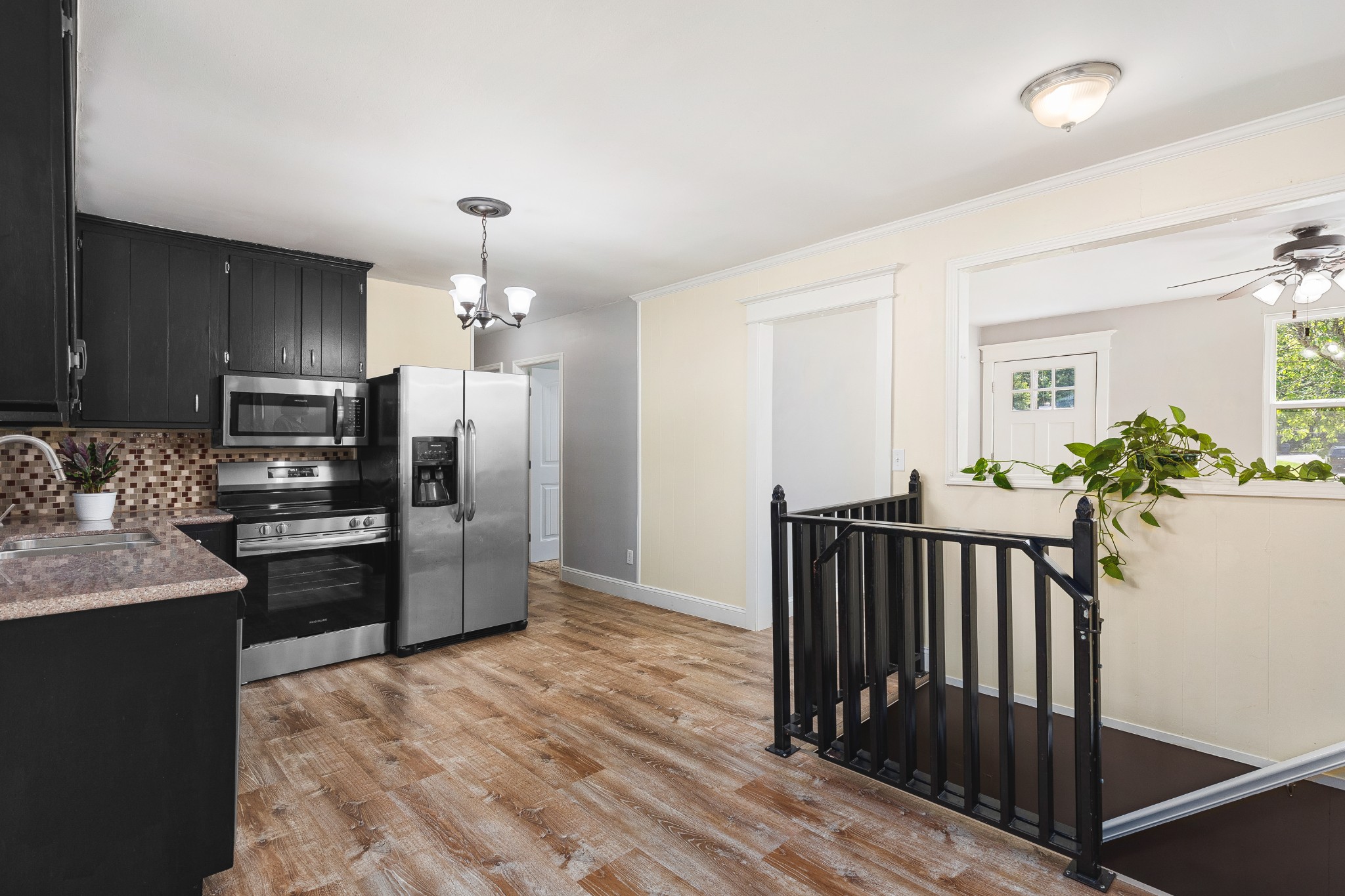 Kitchen with black cabinets and stainless steel appliances beside a black-railed stairwell.