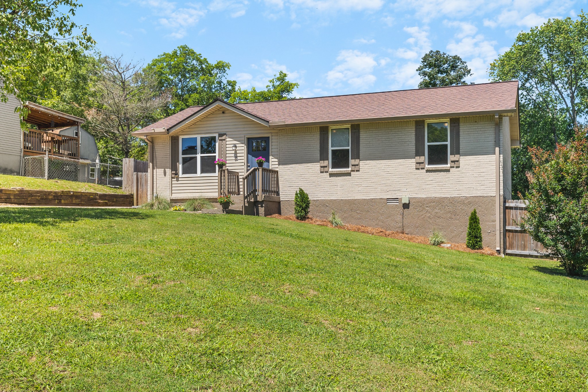 Side view of a single-story beige house with a small porch and broad sloping lawn.
