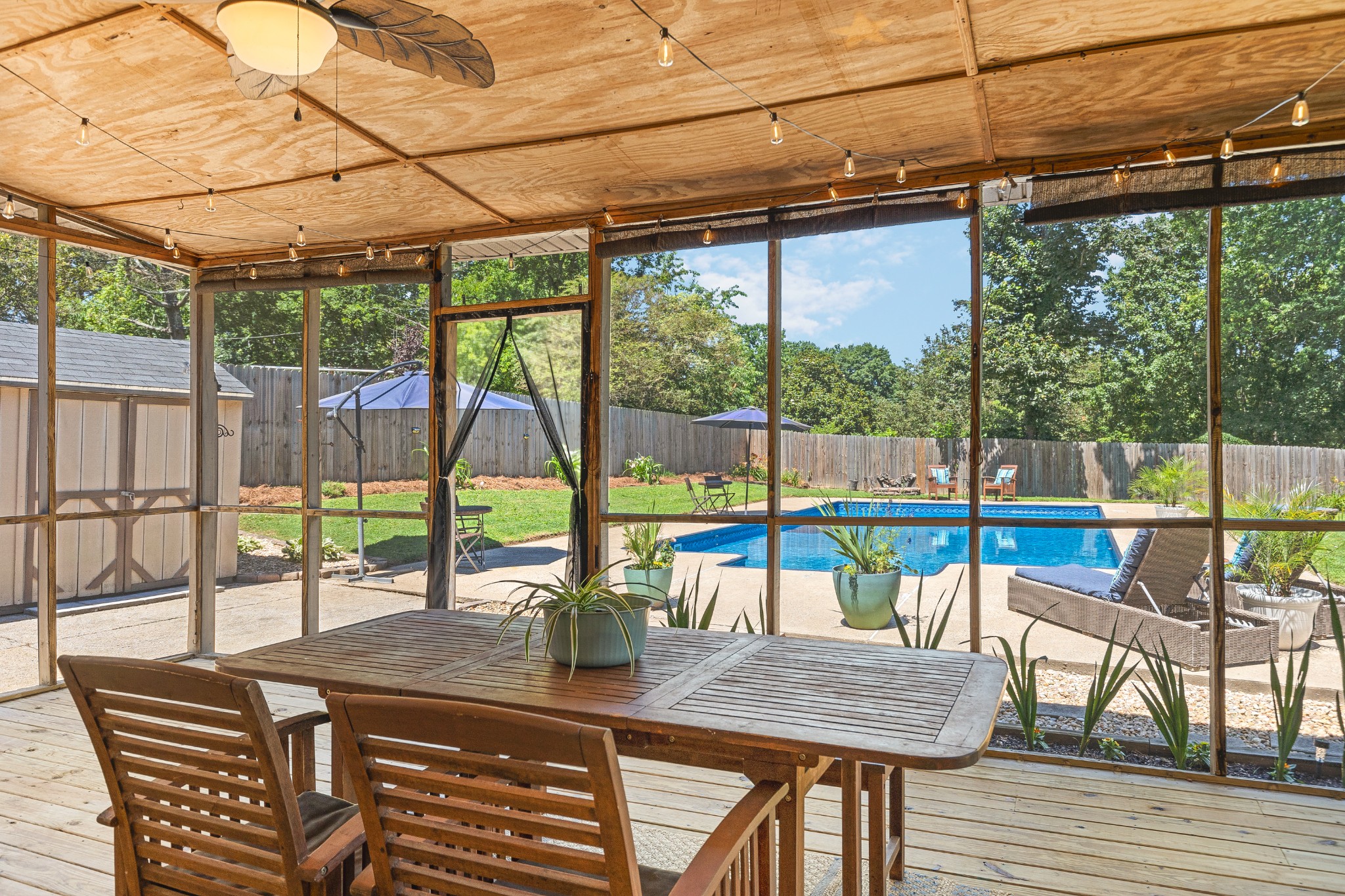 Screened porch with a wooden dining table overlooking a backyard pool.