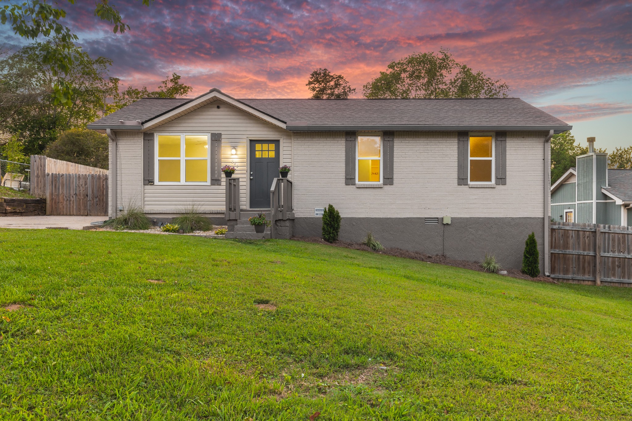 Single-story gray house with a small front porch and broad lawn under a colorful dusk sky.