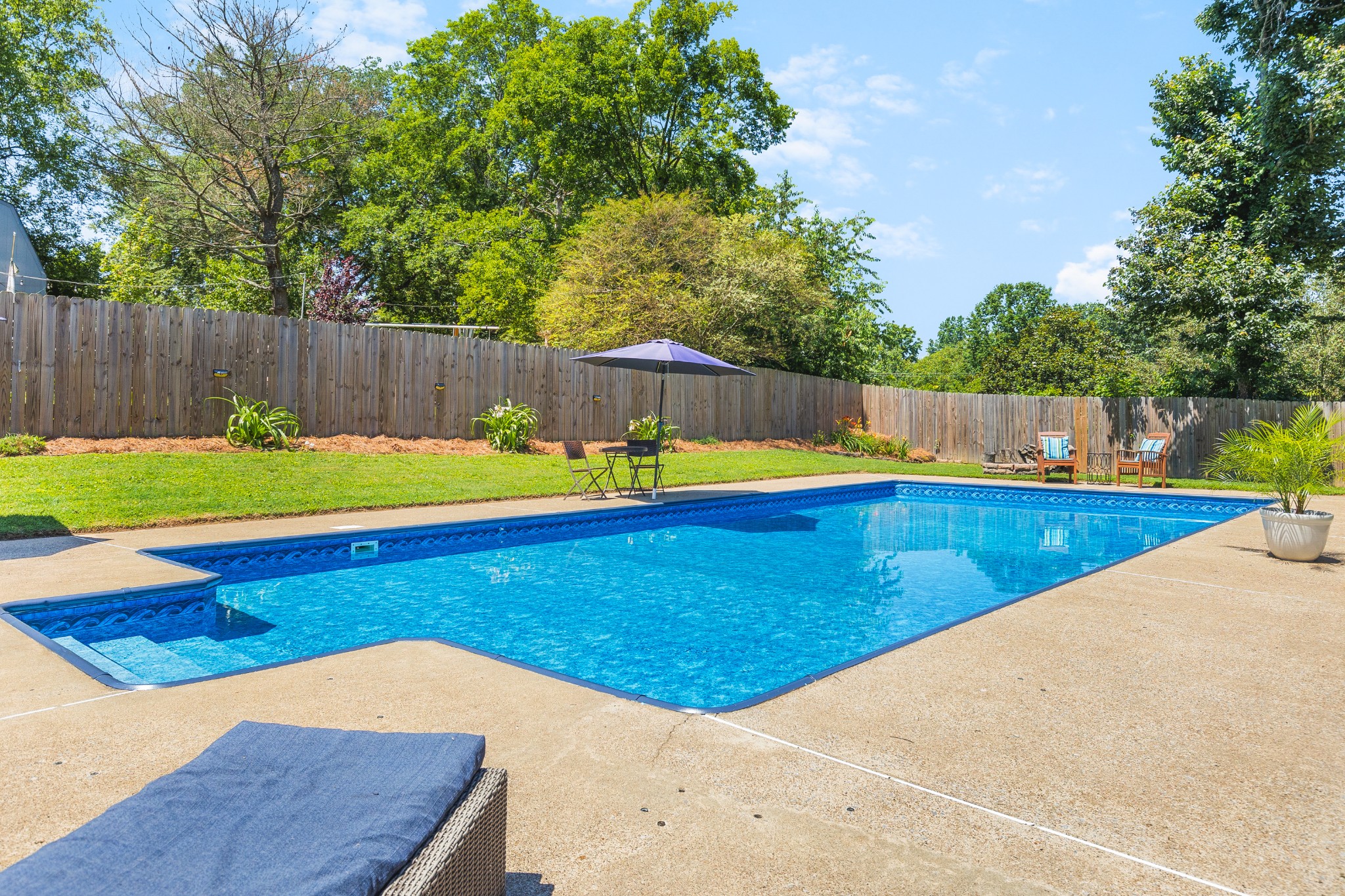 Backyard swimming pool with a concrete deck, fenced lawn, and patio seating.