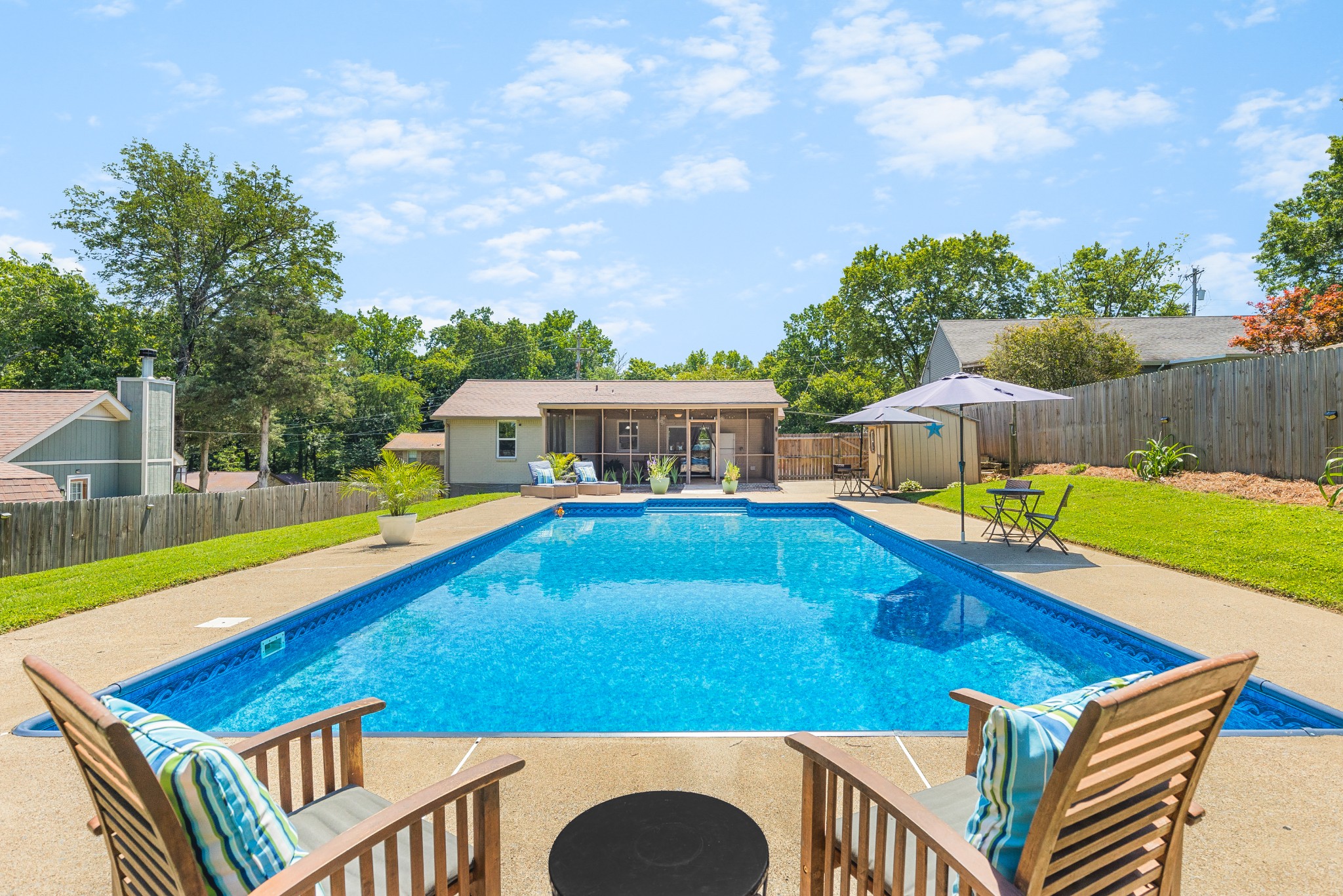 Backyard pool with a concrete deck, wooden lounge chairs, and a screened porch.
