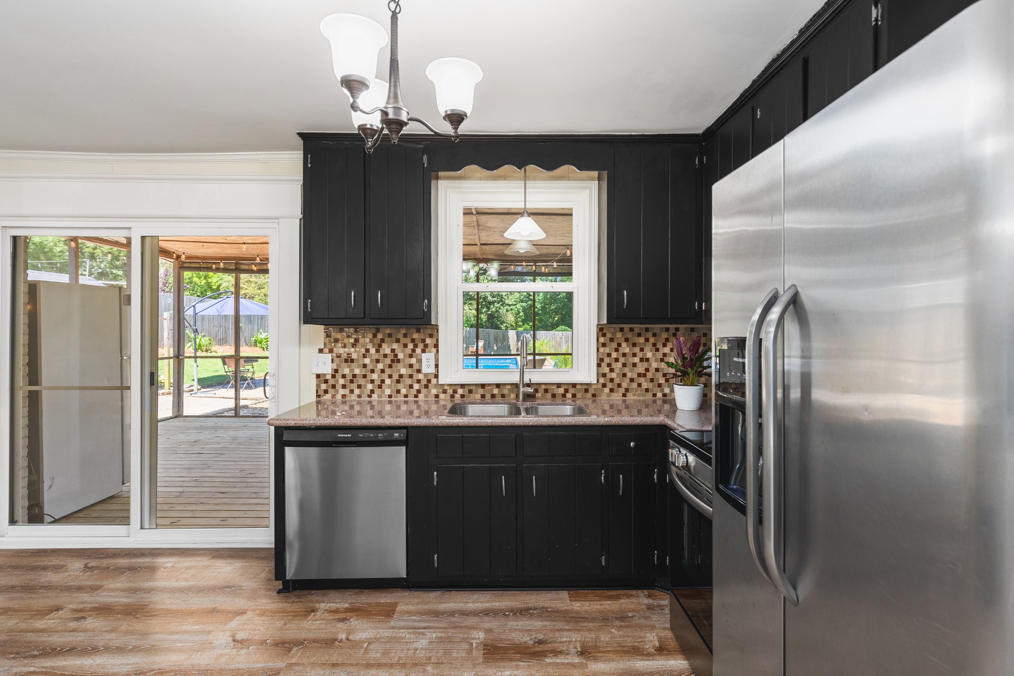 Kitchen with black cabinets, stainless steel appliances, and a mosaic backsplash, opening onto a covered deck.