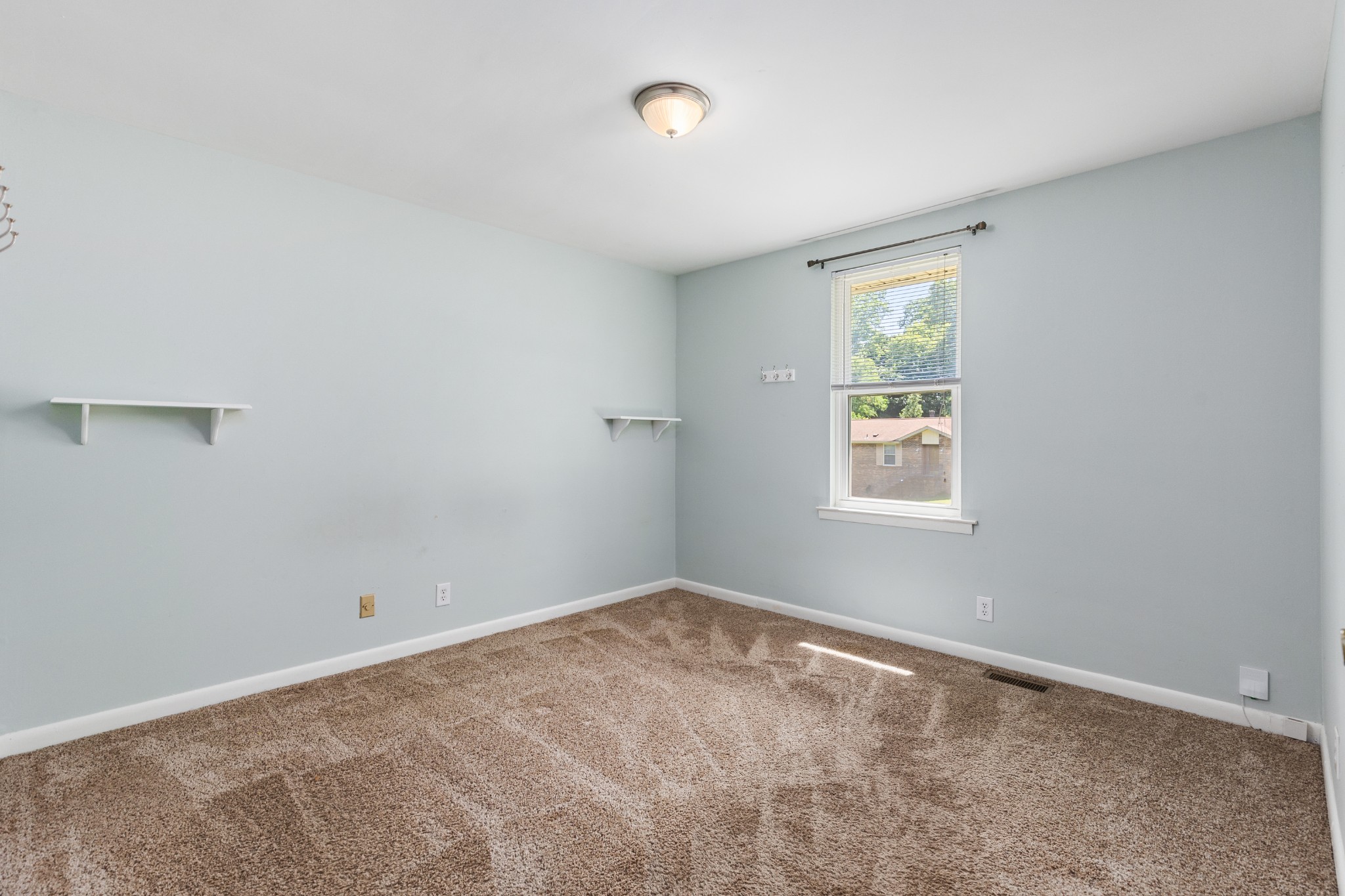 Empty bedroom with beige carpet, pale blue-gray walls, and a window with blinds.