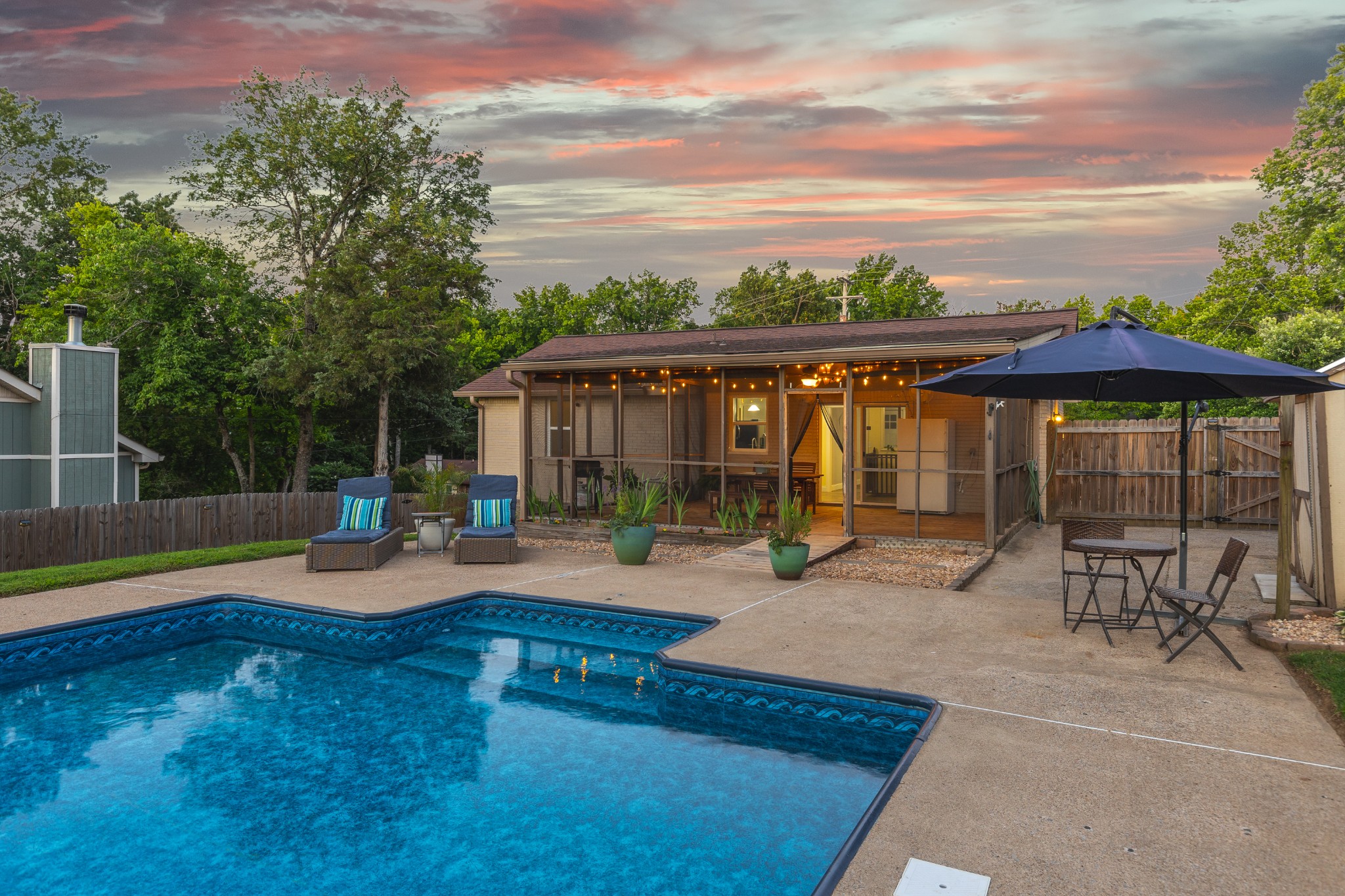 Backyard pool and furnished patio in front of a home with a covered porch at dusk.