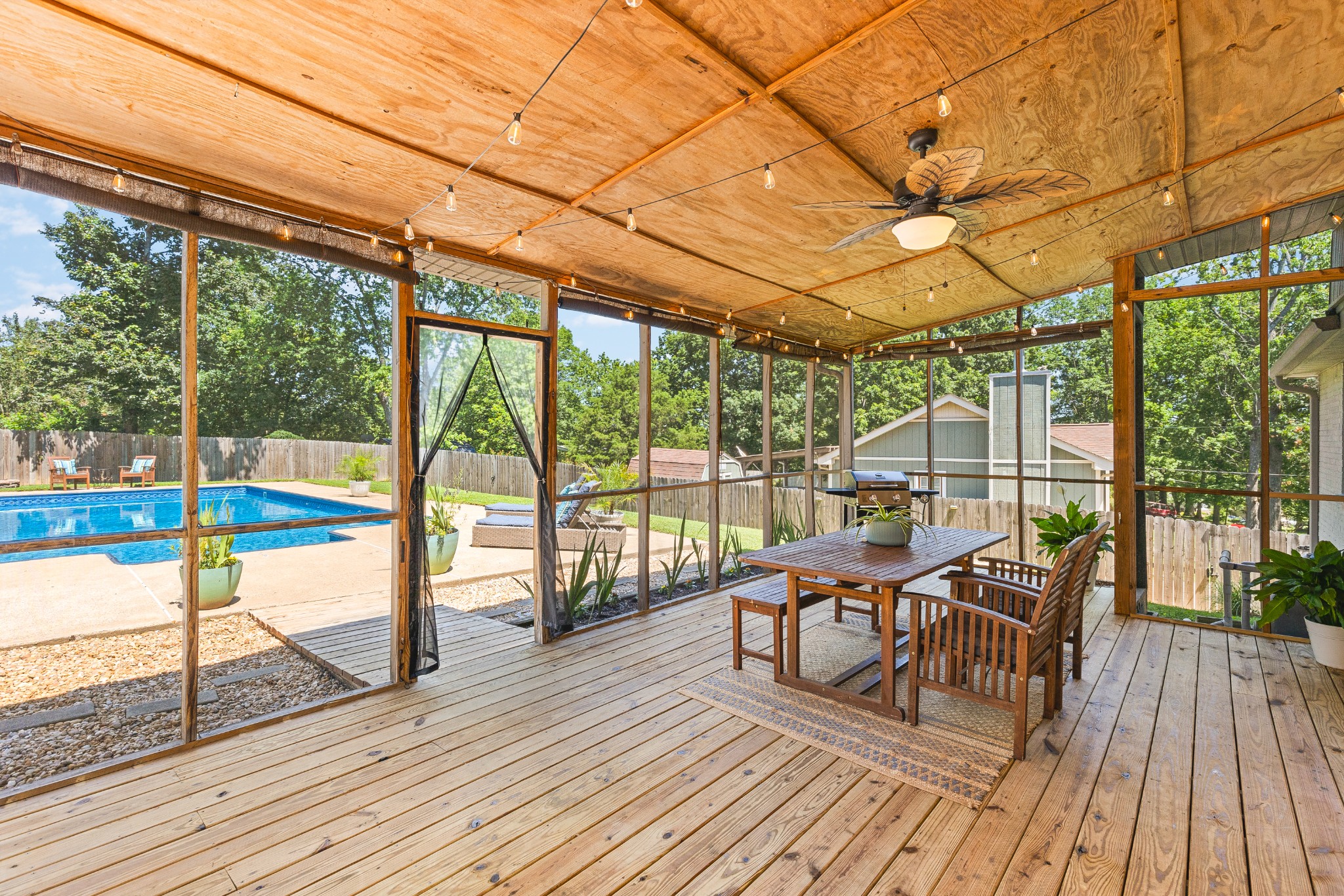 Screened wooden patio with dining furniture overlooking a backyard pool.
