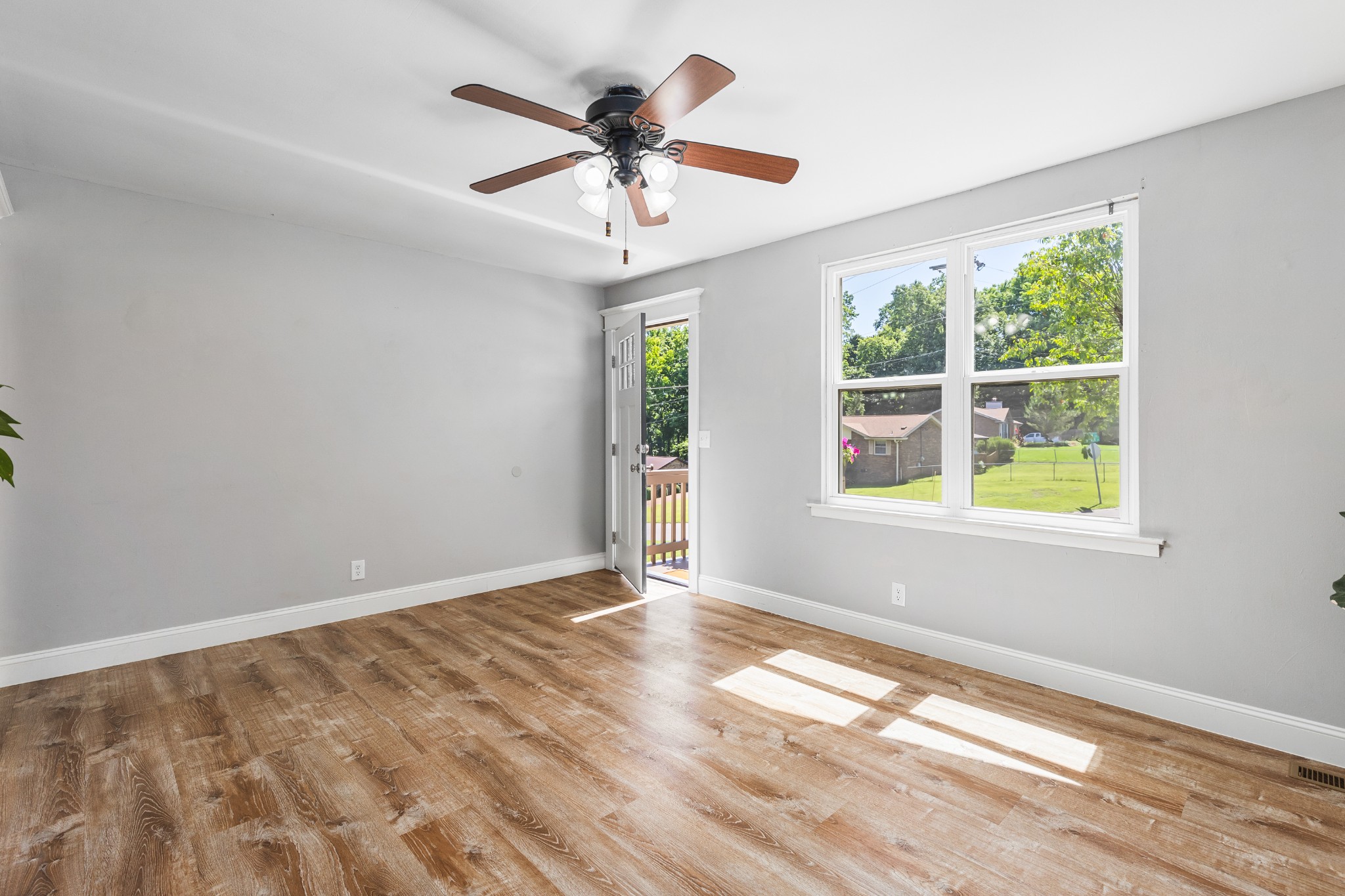 Vacant room with wood-look flooring, a ceiling fan, and a window overlooking a green yard.
