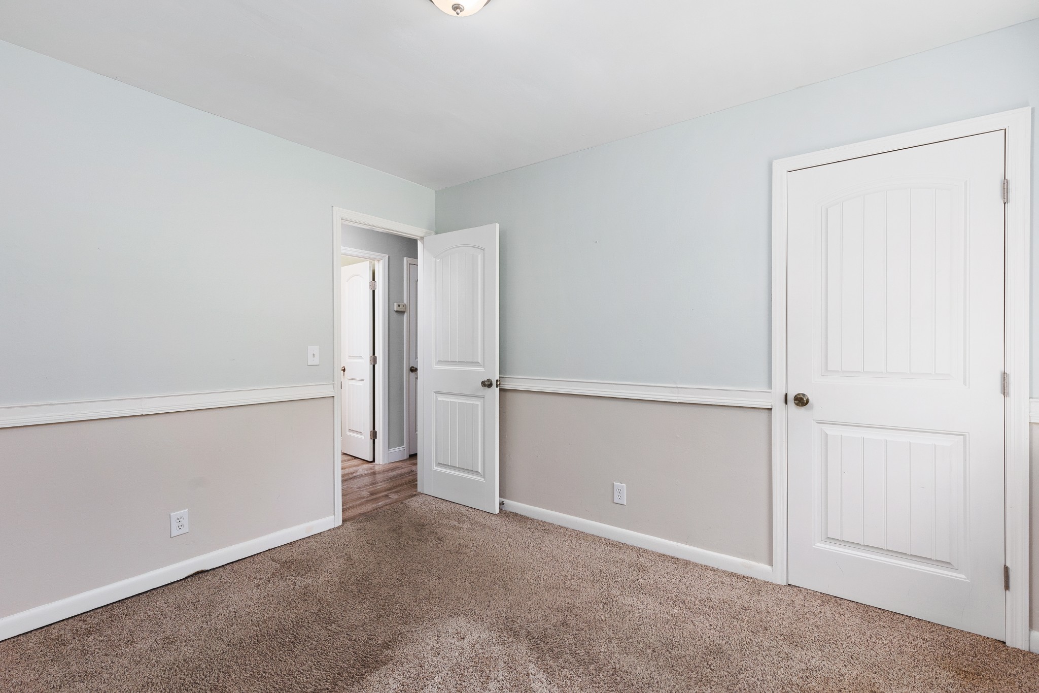 Empty carpeted room with pale blue walls, white trim, and an open doorway to the hall.