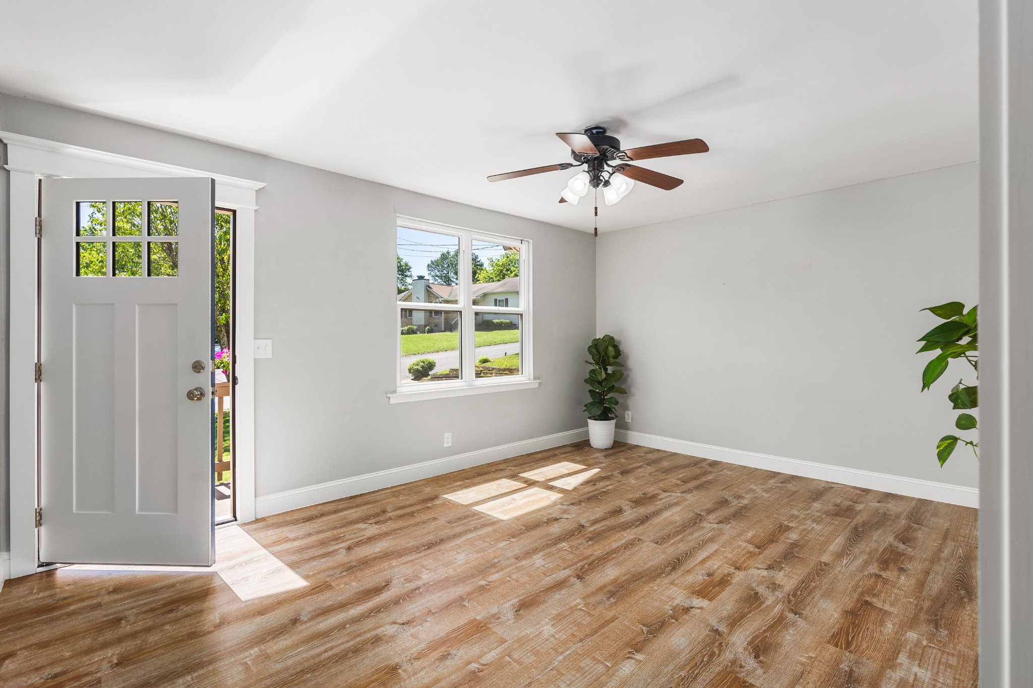 Vacant room with wood-look floors, an open front door, and a ceiling fan.