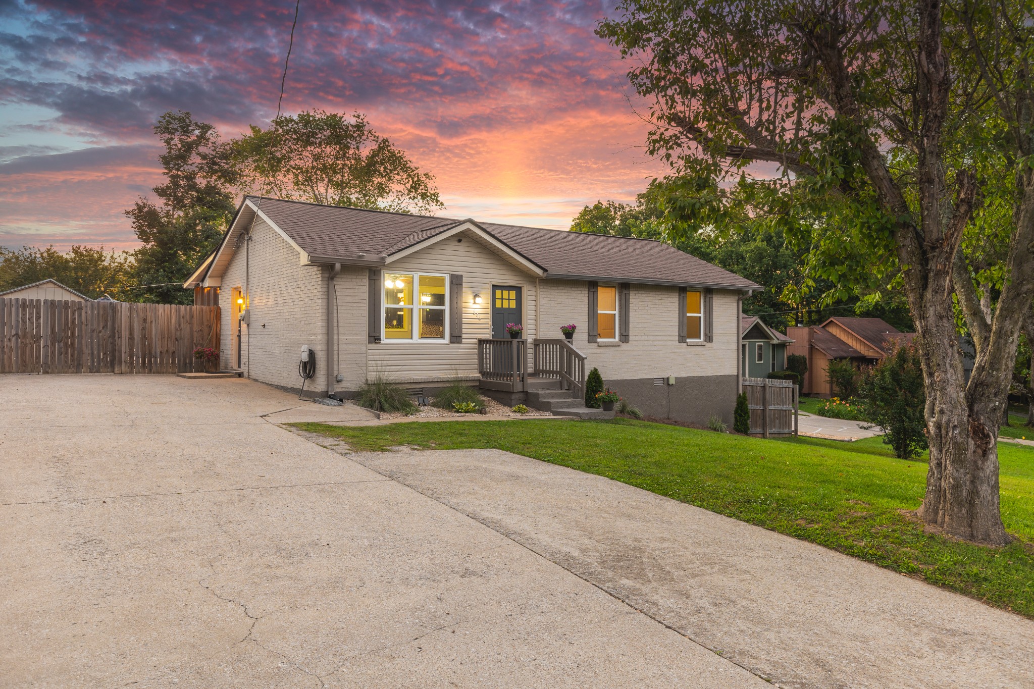 Single-story brick house with a small entry porch and broad driveway beneath a colorful sunset sky.