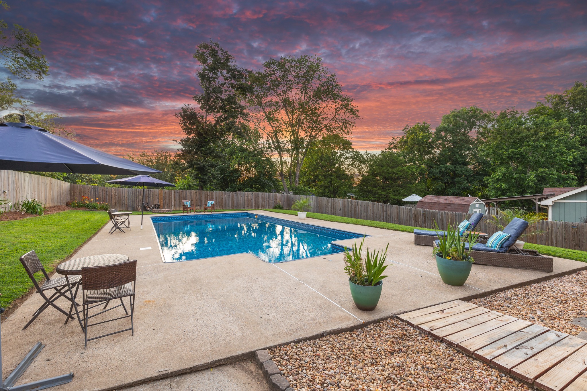 Backyard pool and patio seating beneath a vivid pink-orange sunset sky.