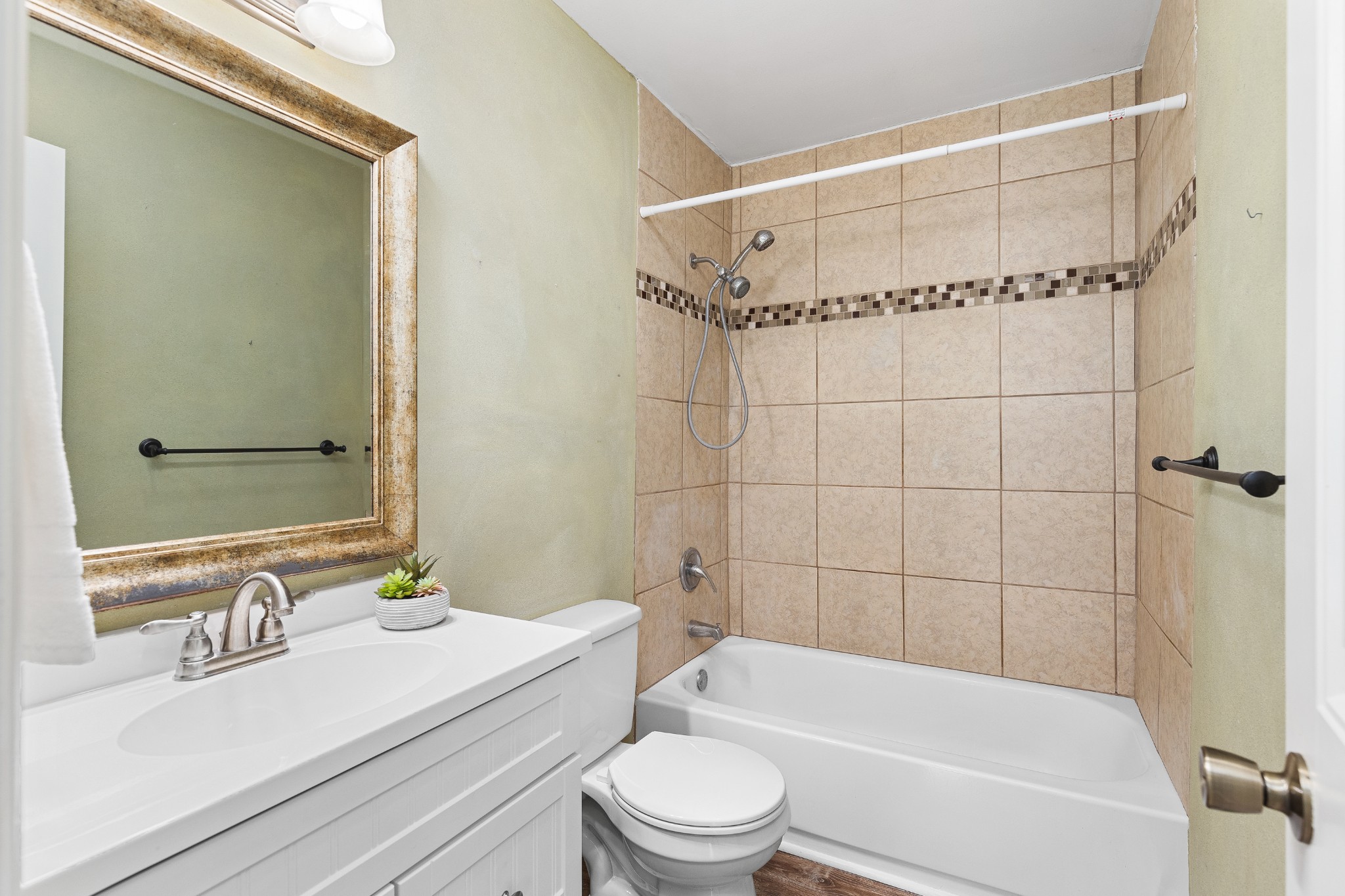 Bathroom with white vanity, toilet, and bathtub beneath a tan tiled shower surround.