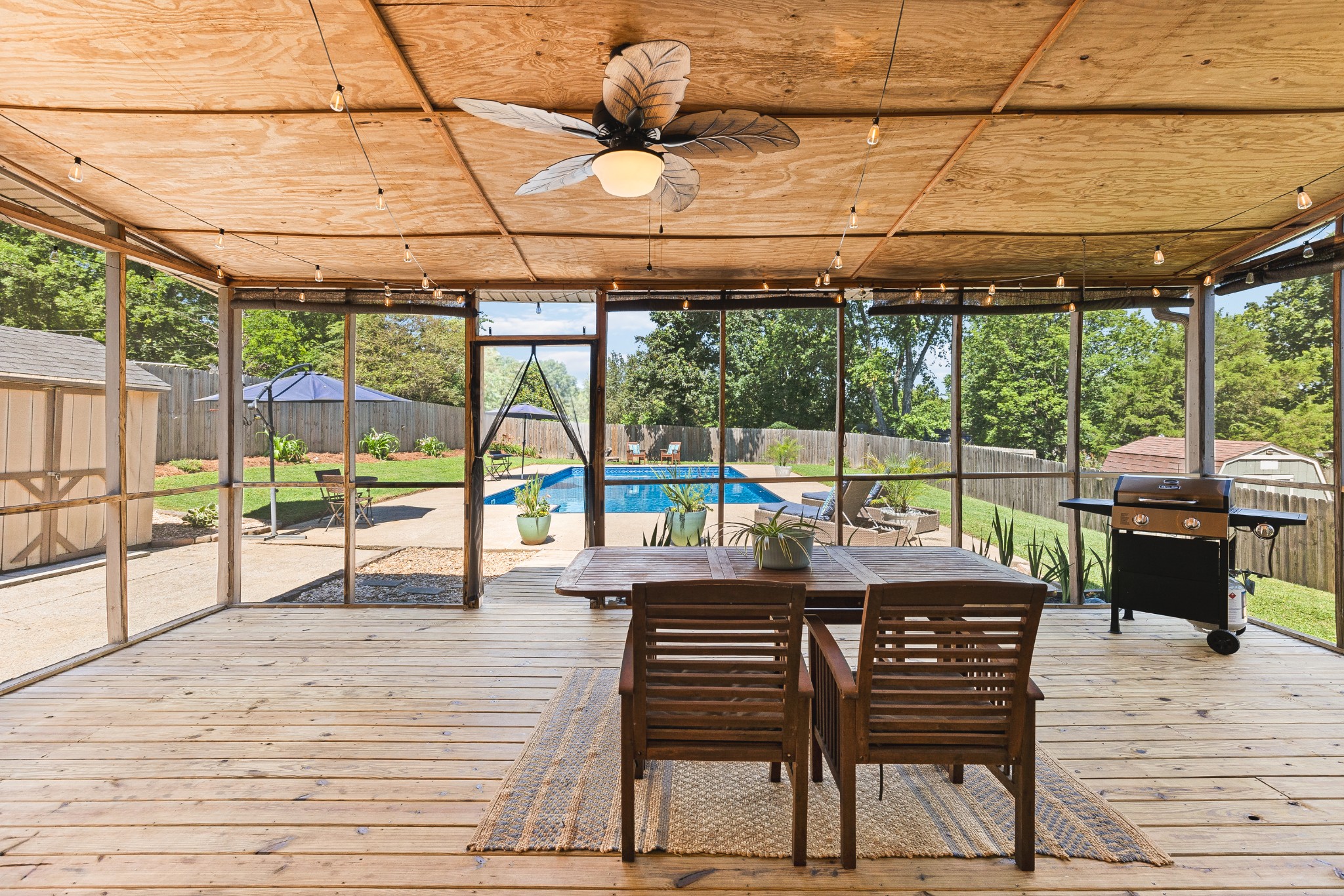 Screened patio with wooden dining set and grill overlooking a backyard pool.