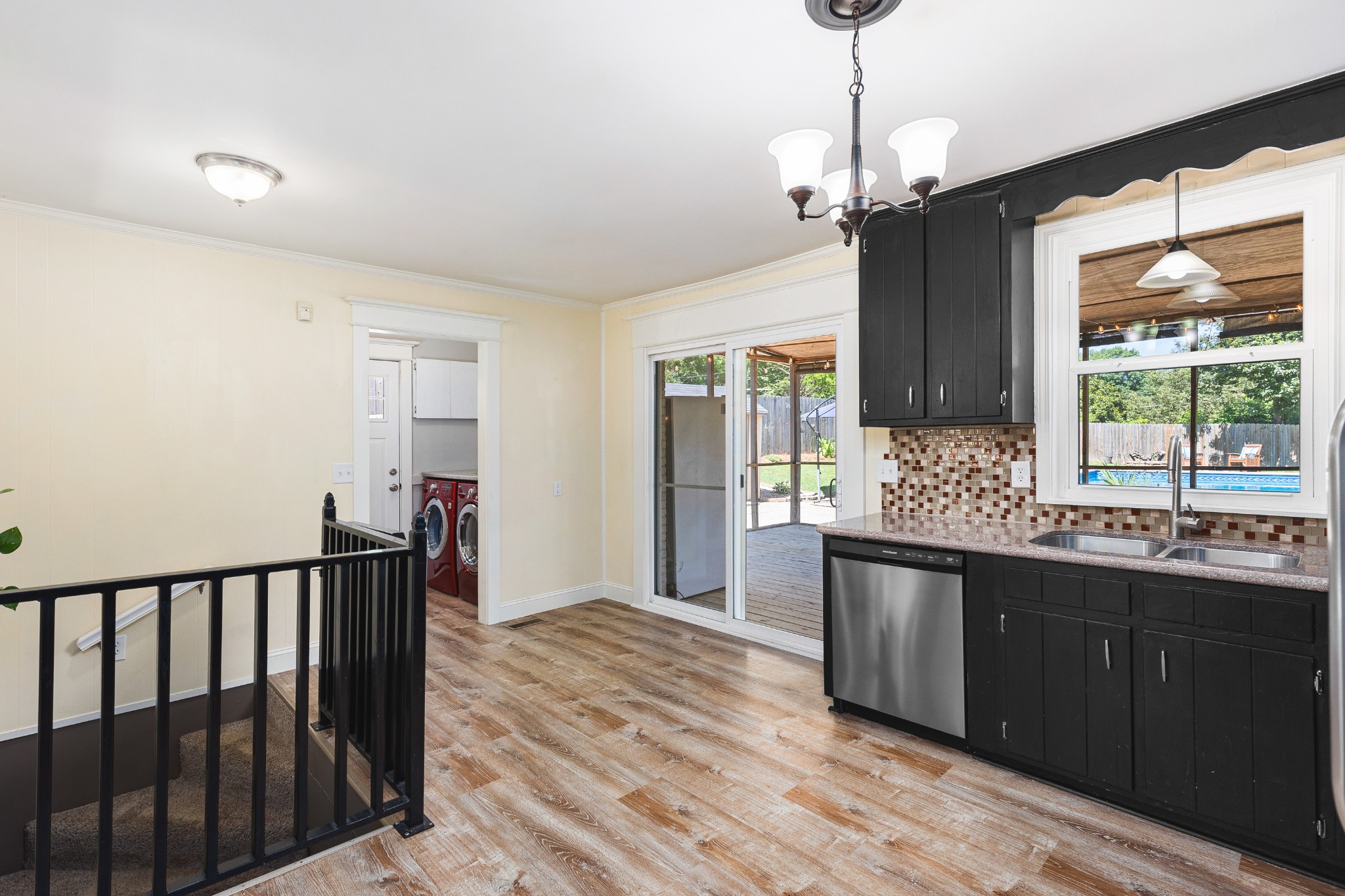 Kitchen with black cabinets and mosaic backsplash, opening to a deck with a pool view.