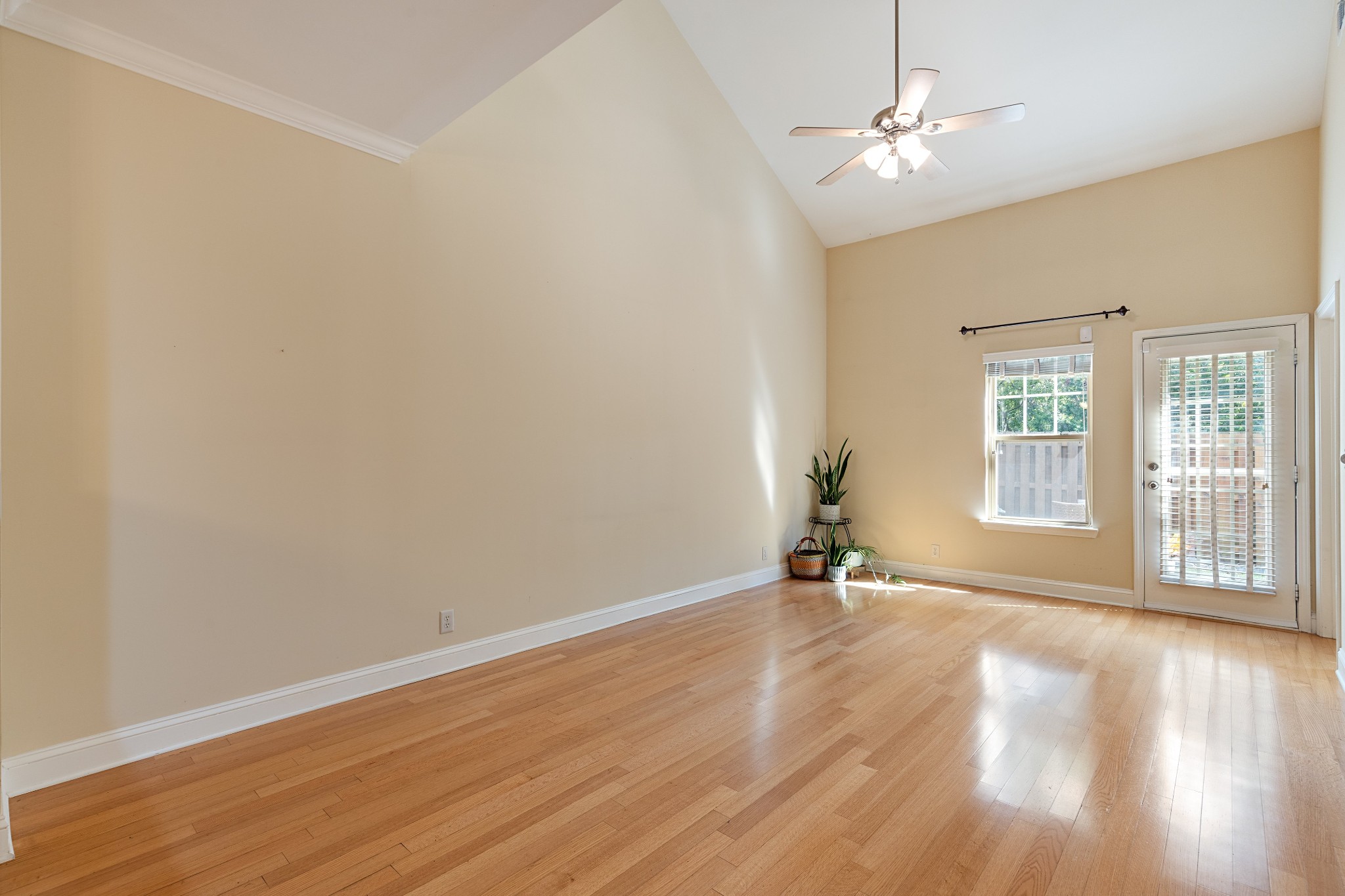 Mostly empty living room with hardwood floors, a high ceiling, and a glass patio door.