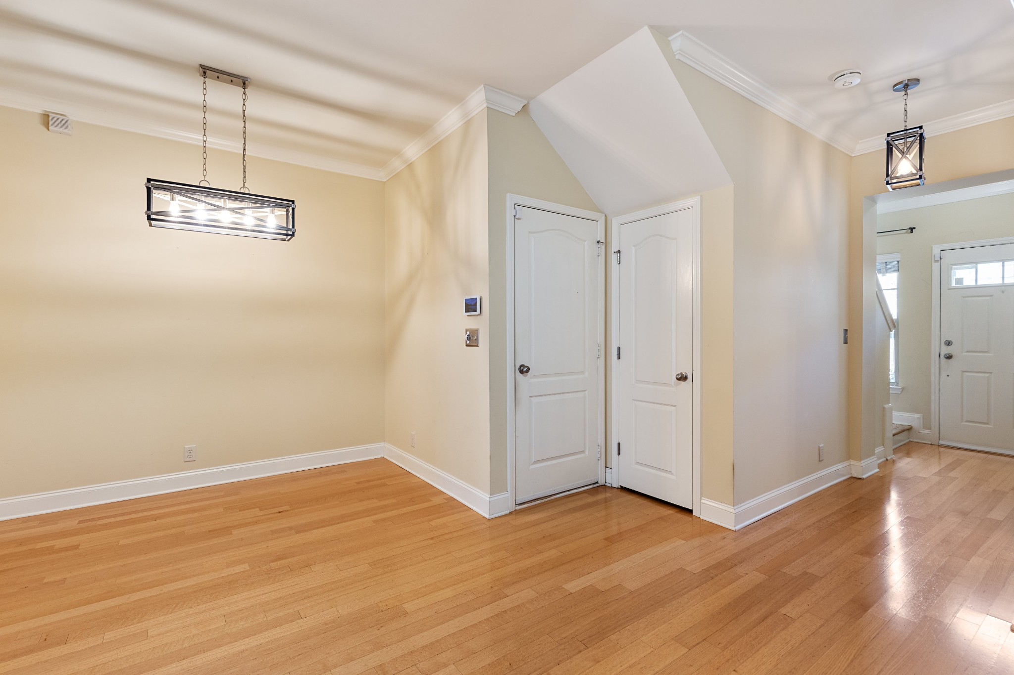 Empty dining area with hardwood floors, a rectangular pendant light, and two white doors.