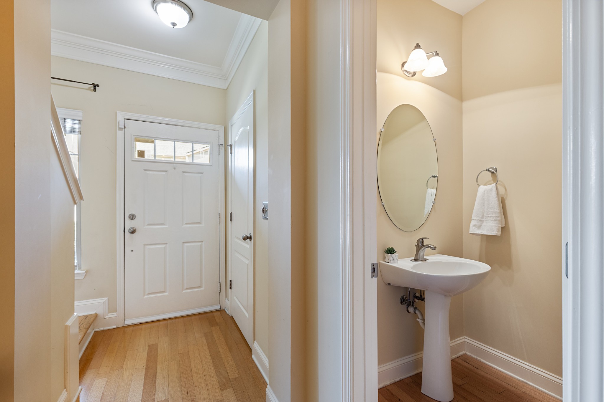 Entry hall with hardwood floors and white front door beside a powder room with pedestal sink.
