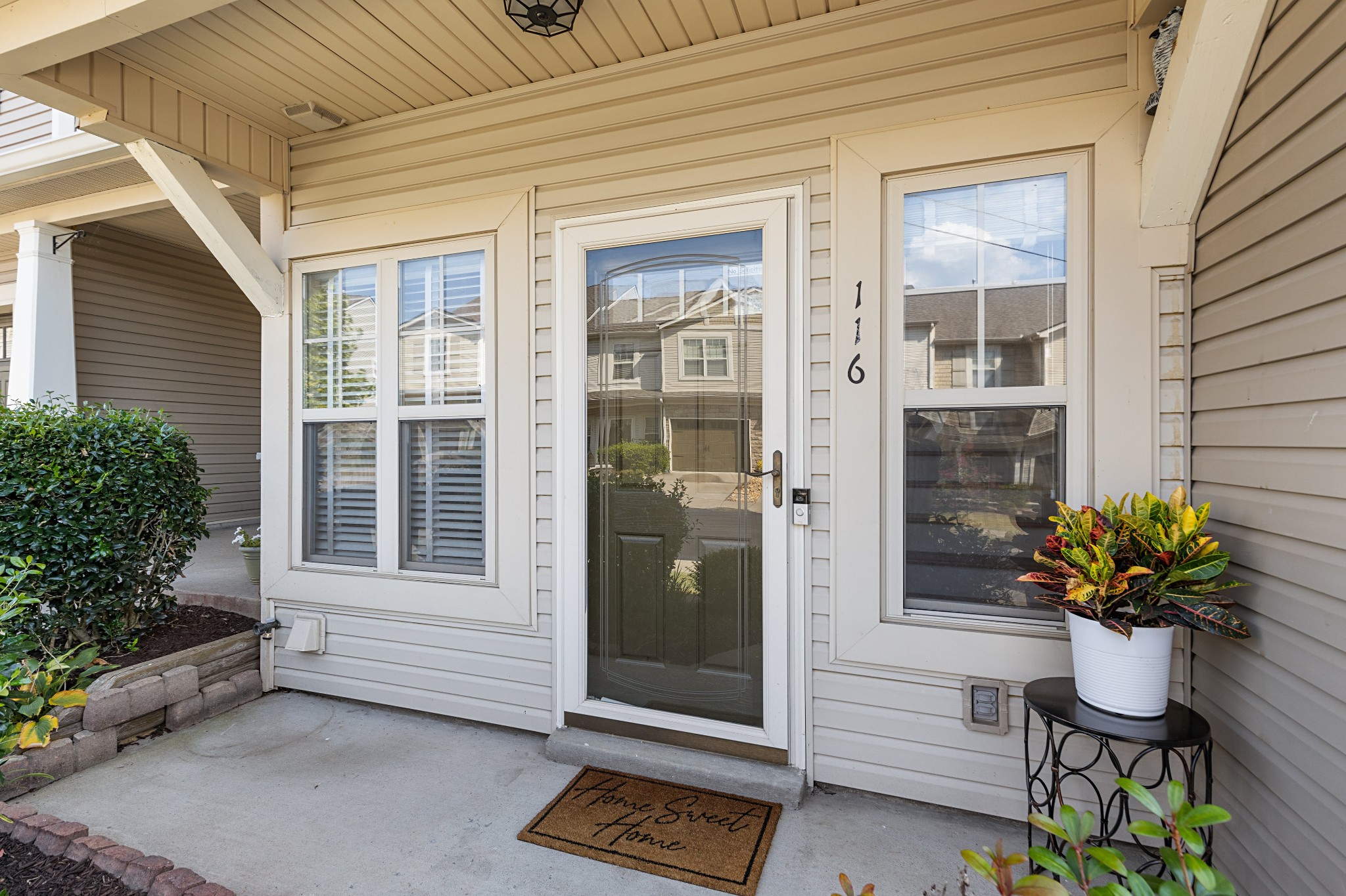 Townhouse front entry with a covered porch, glass storm door, and potted plant beside unit number 116.
