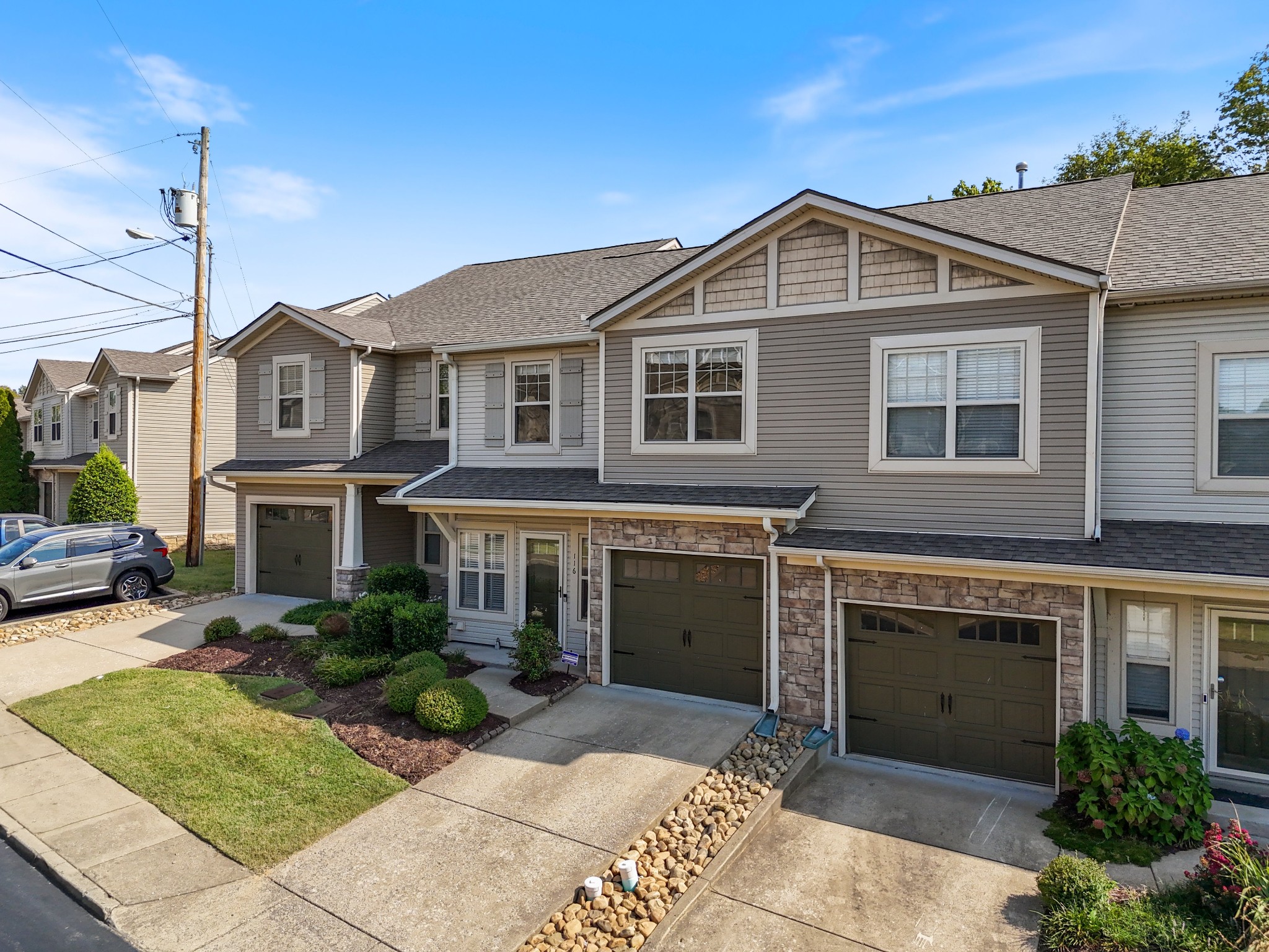 Gray attached townhouse with stone accents, a two-car garage, driveway, and landscaped front lawn.
