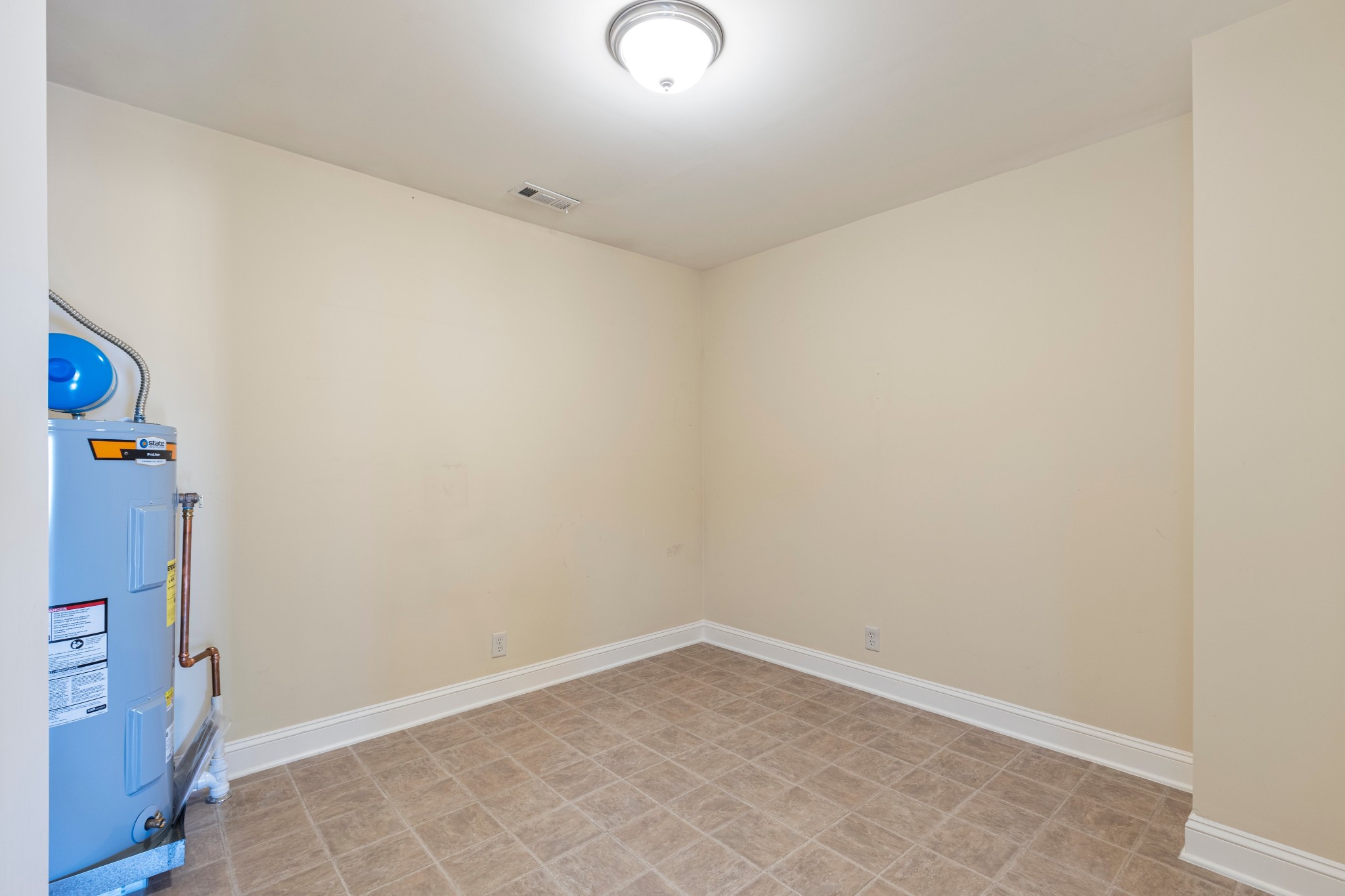 Empty utility room with tan tile flooring and a blue water heater.