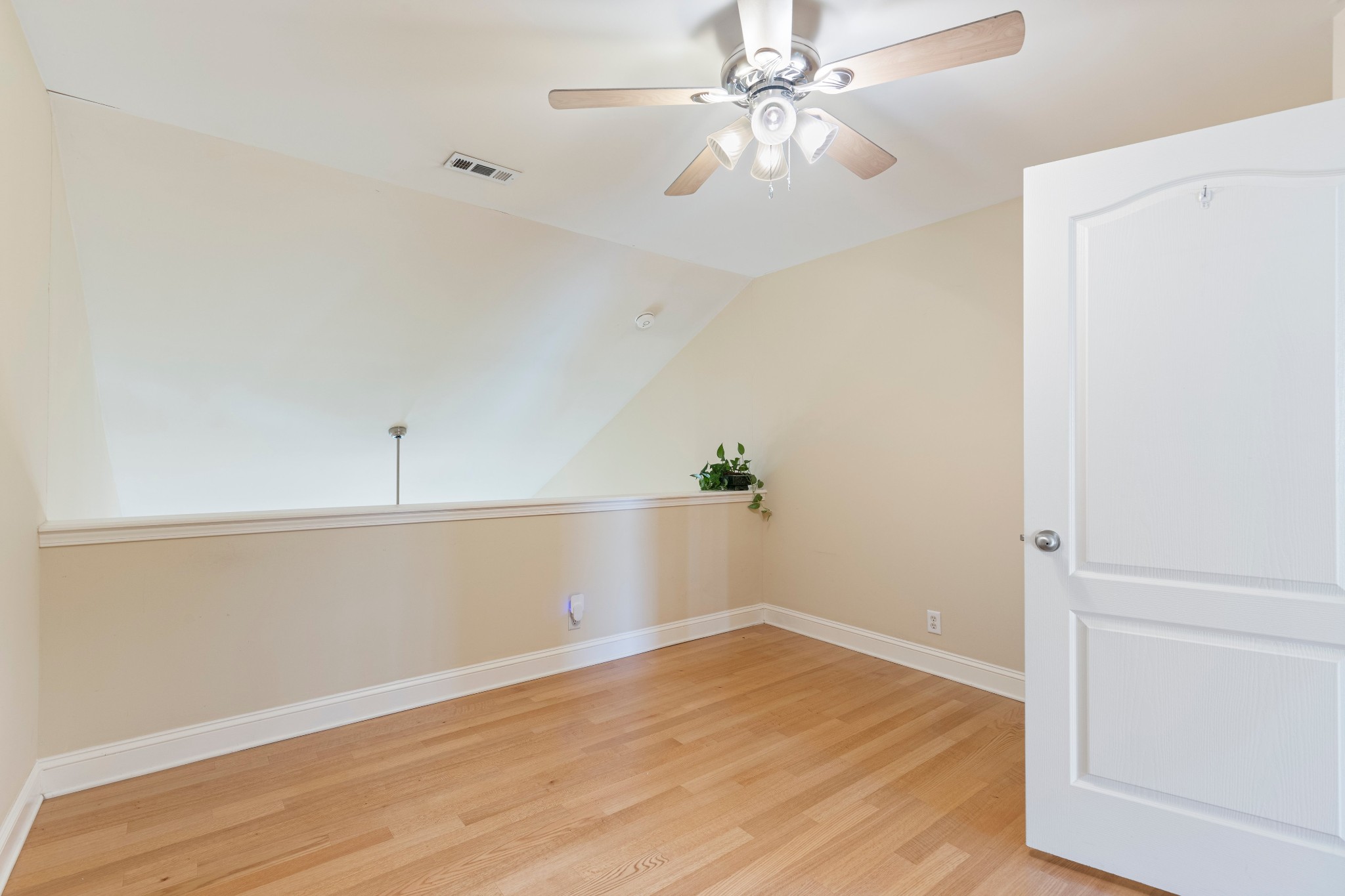 Unfurnished upstairs loft with hardwood floors, a half wall, and a ceiling fan.