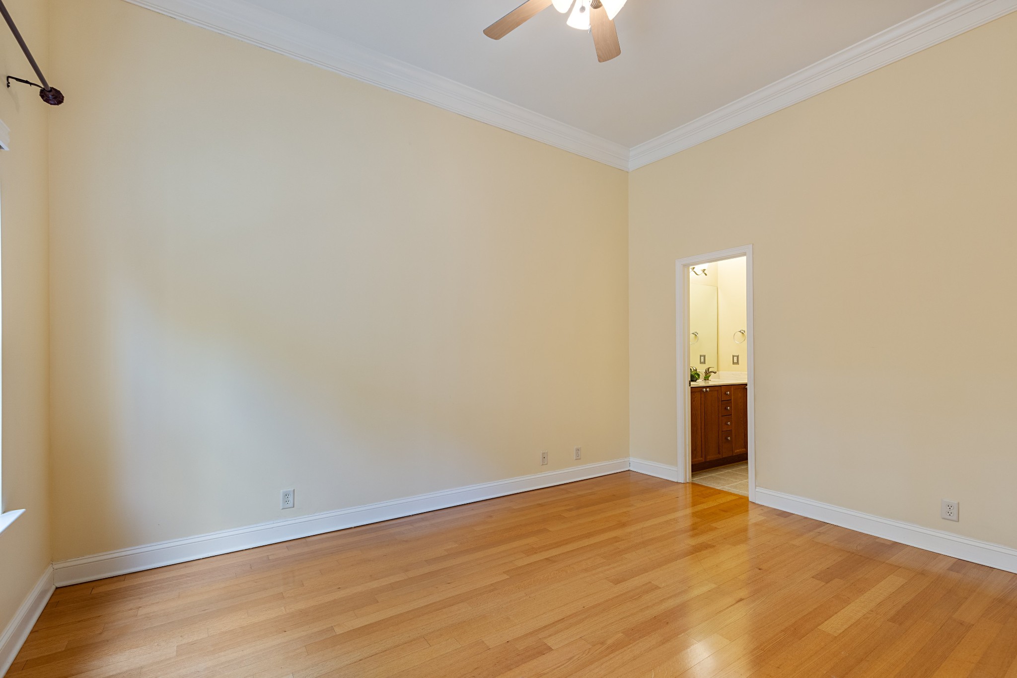 Empty bedroom with hardwood floors and a ceiling fan, opening to a bathroom vanity.