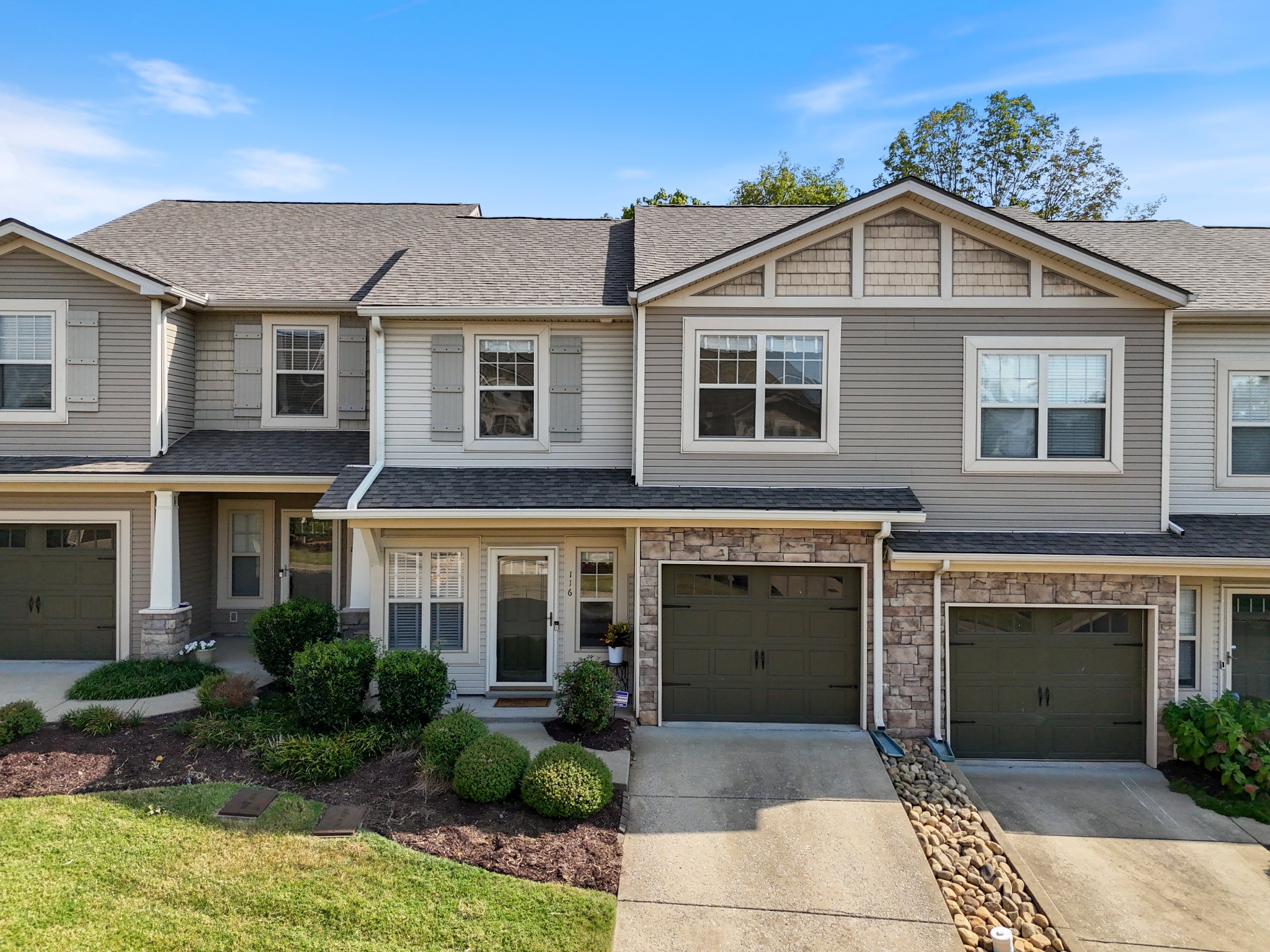 Two-story gray townhouse with stone accents, dark garage door, and landscaped front entry.