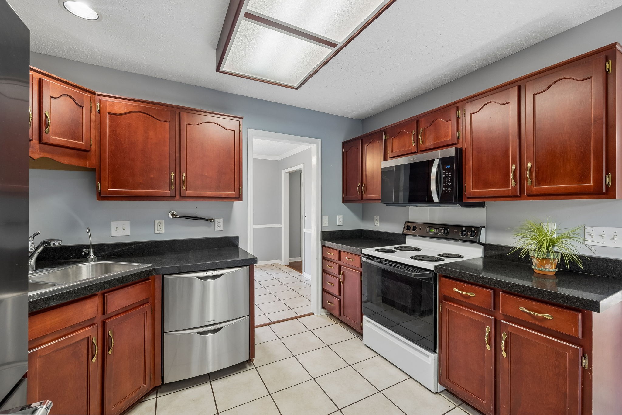 Kitchen with reddish-brown cabinets, black countertops, stainless-steel dishwasher, and white electric range.