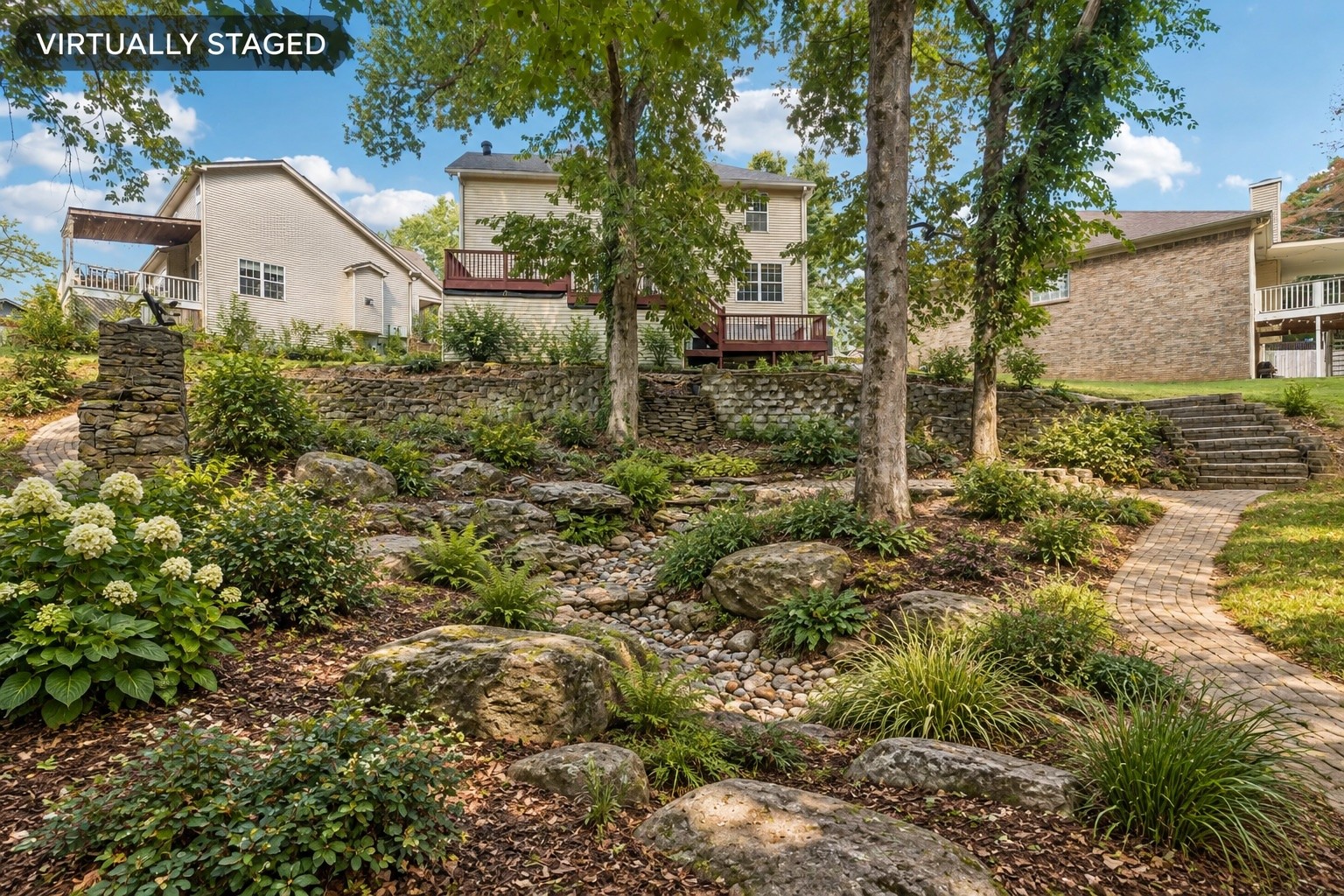 Rear of a two-story home above a landscaped garden with stone walls and a curved walkway.