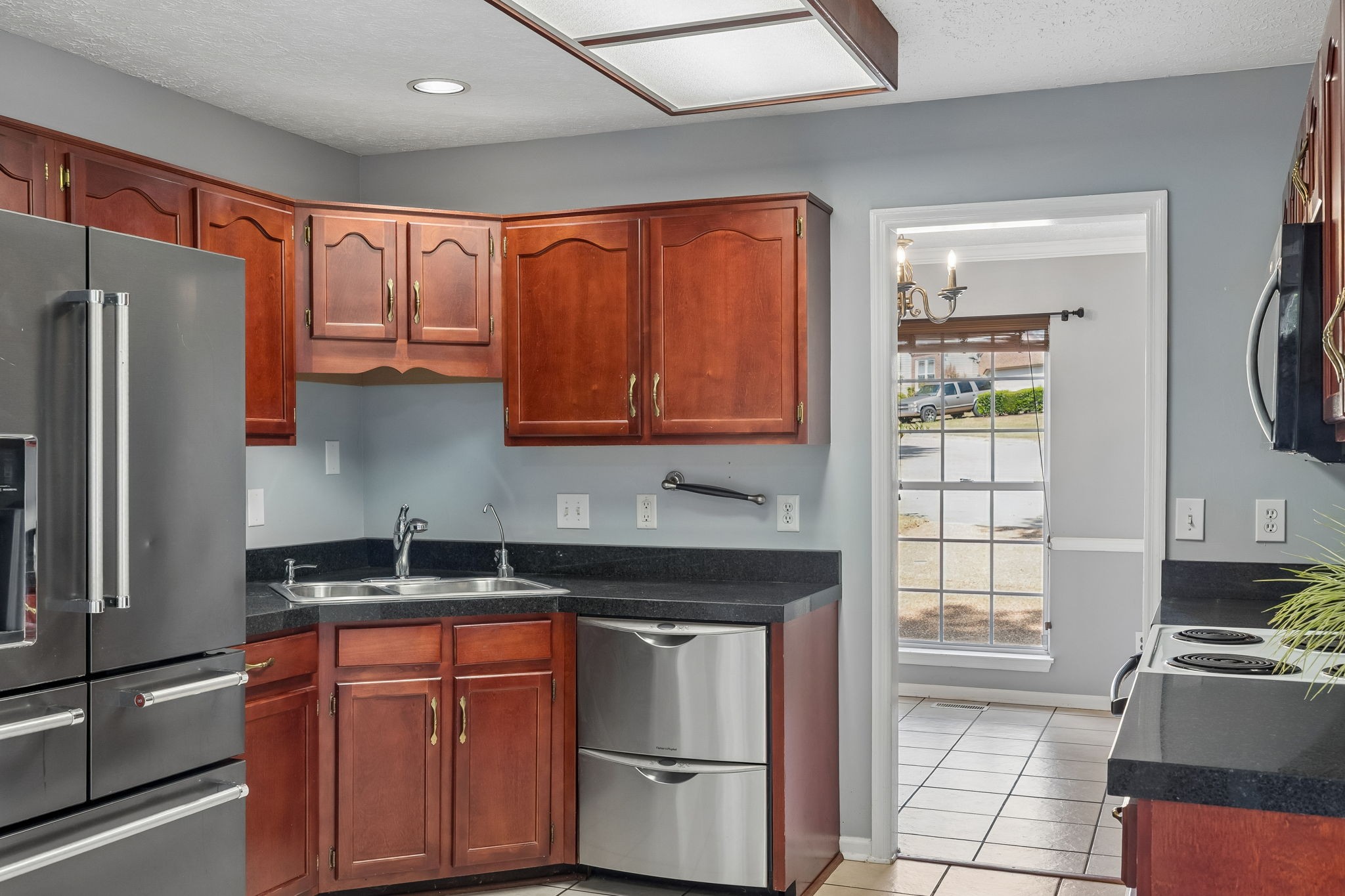 Kitchen with reddish-brown cabinets, dark countertops, stainless steel appliances, and a double-basin sink.