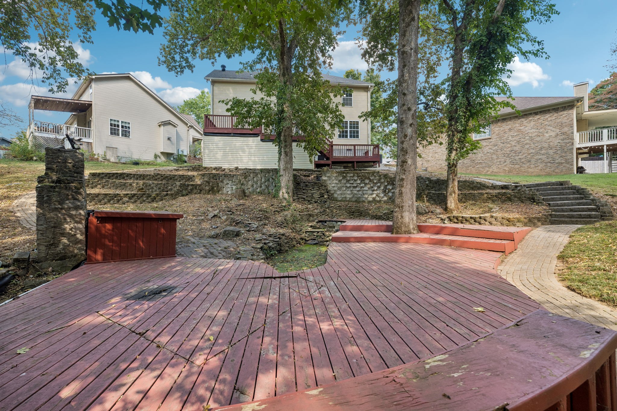 Backyard deck with mature trees, stone retaining walls, and steps leading up to the house.