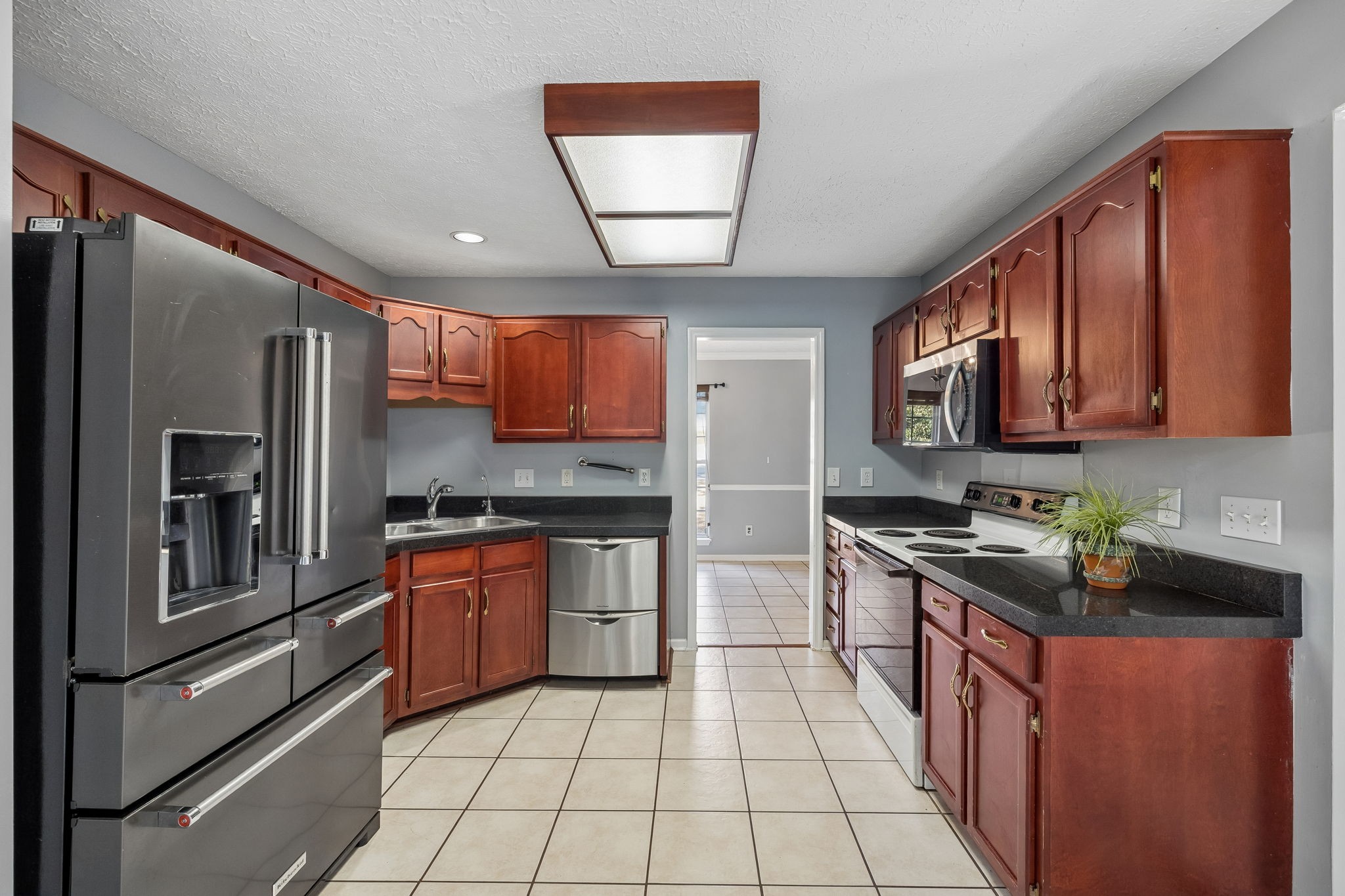 Kitchen with reddish-brown cabinets, black countertops, stainless steel appliances, and light tile flooring.