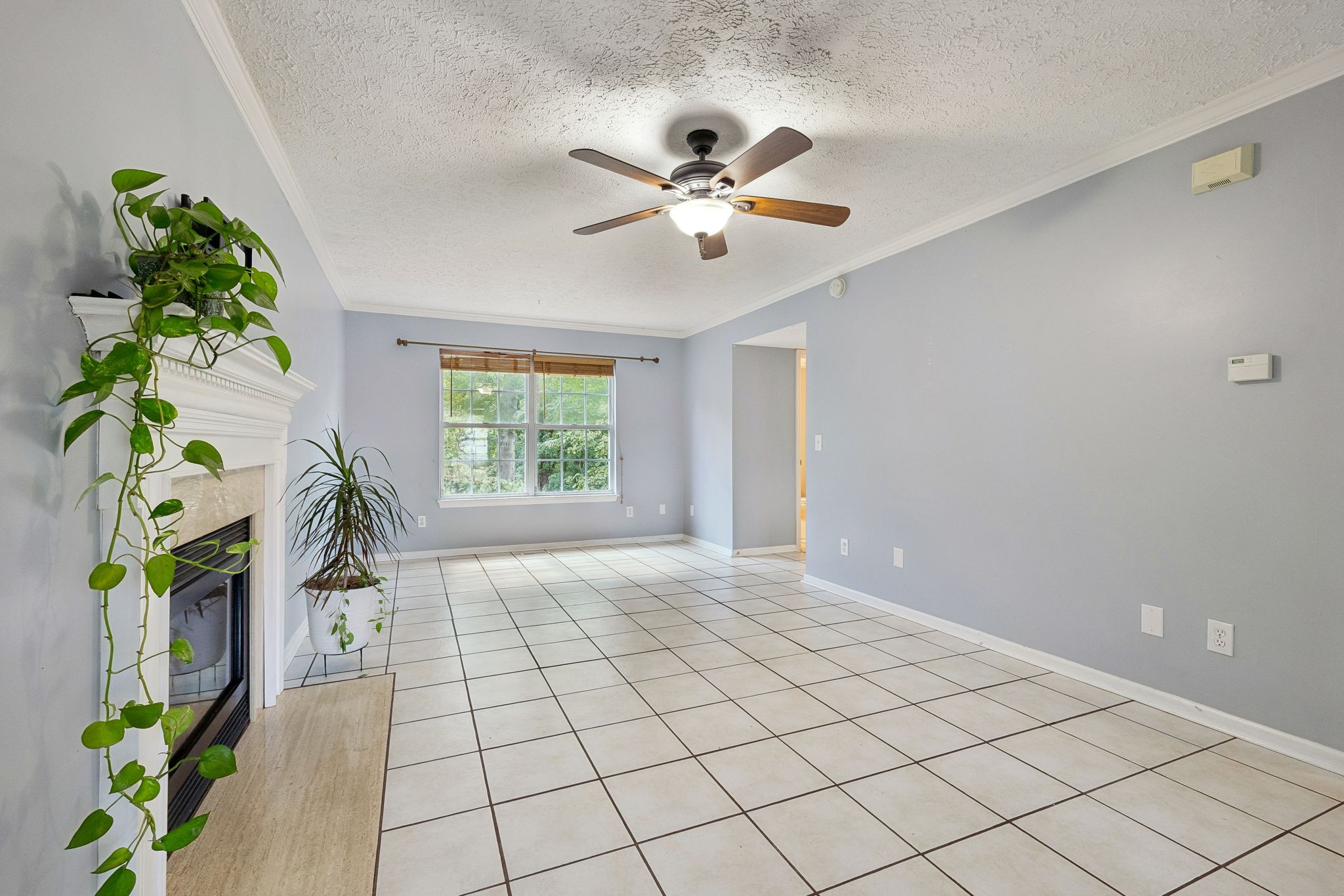 Living room with a tiled floor, white-mantel fireplace, ceiling fan, and window with bamboo blinds.
